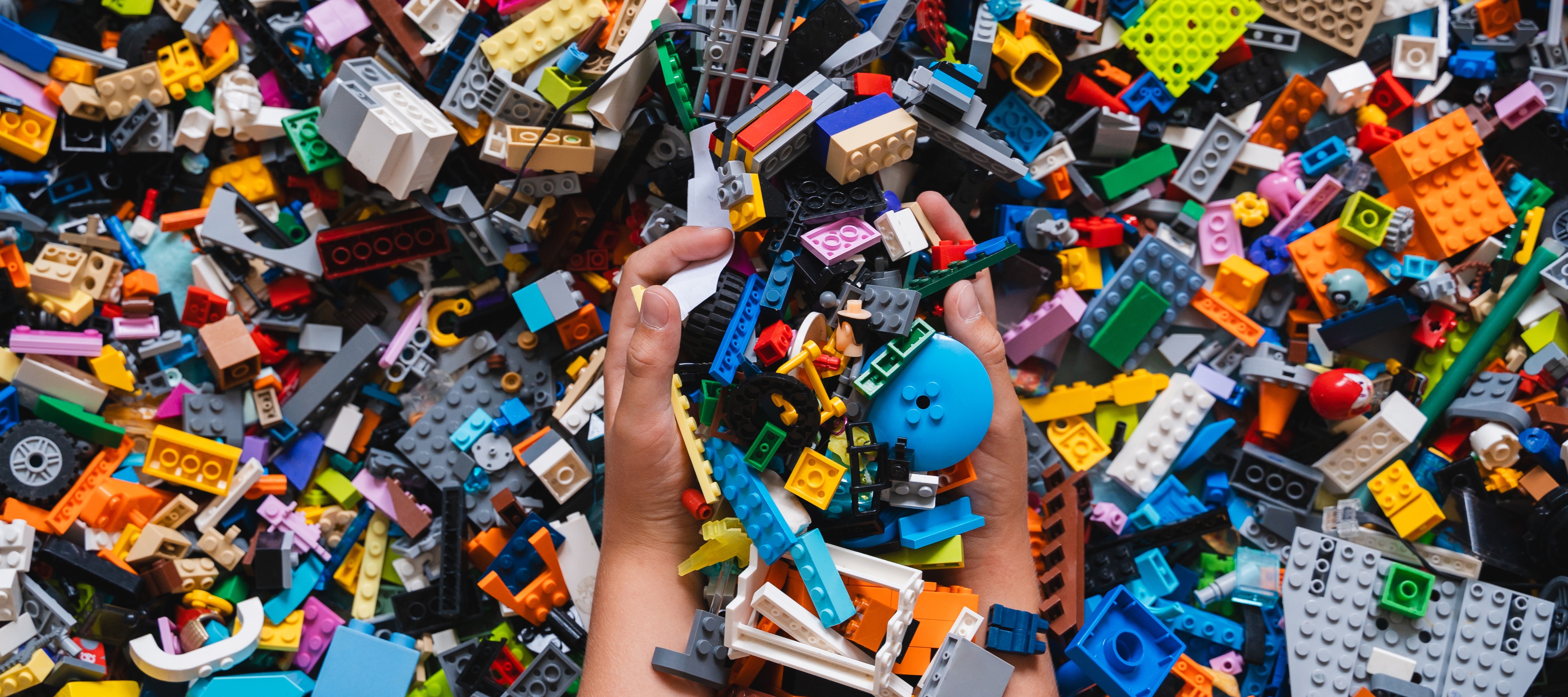 Hands hold a collection of colorful building blocks, presenting a vibrant array of shapes and colors including blue, orange, gray, and black.