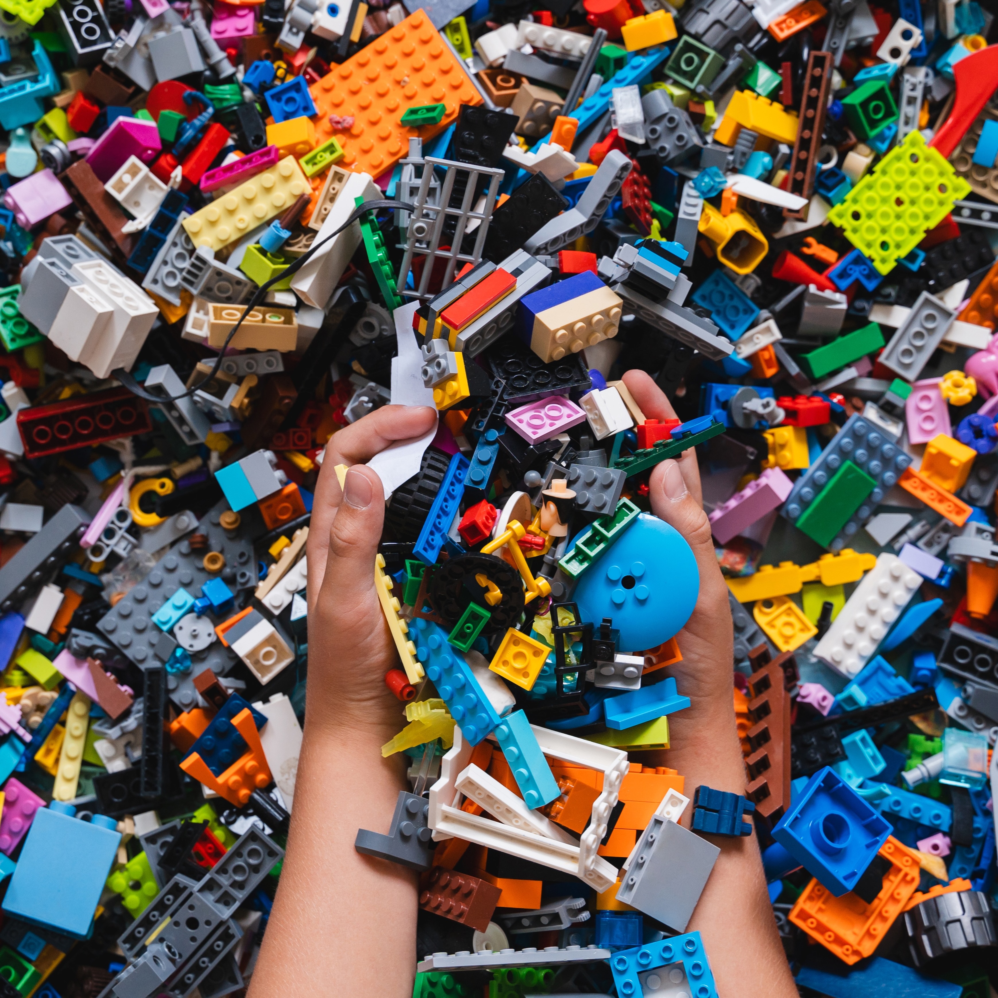 Hands hold a collection of colorful building blocks, presenting a vibrant array of shapes and colors including blue, orange, gray, and black.
