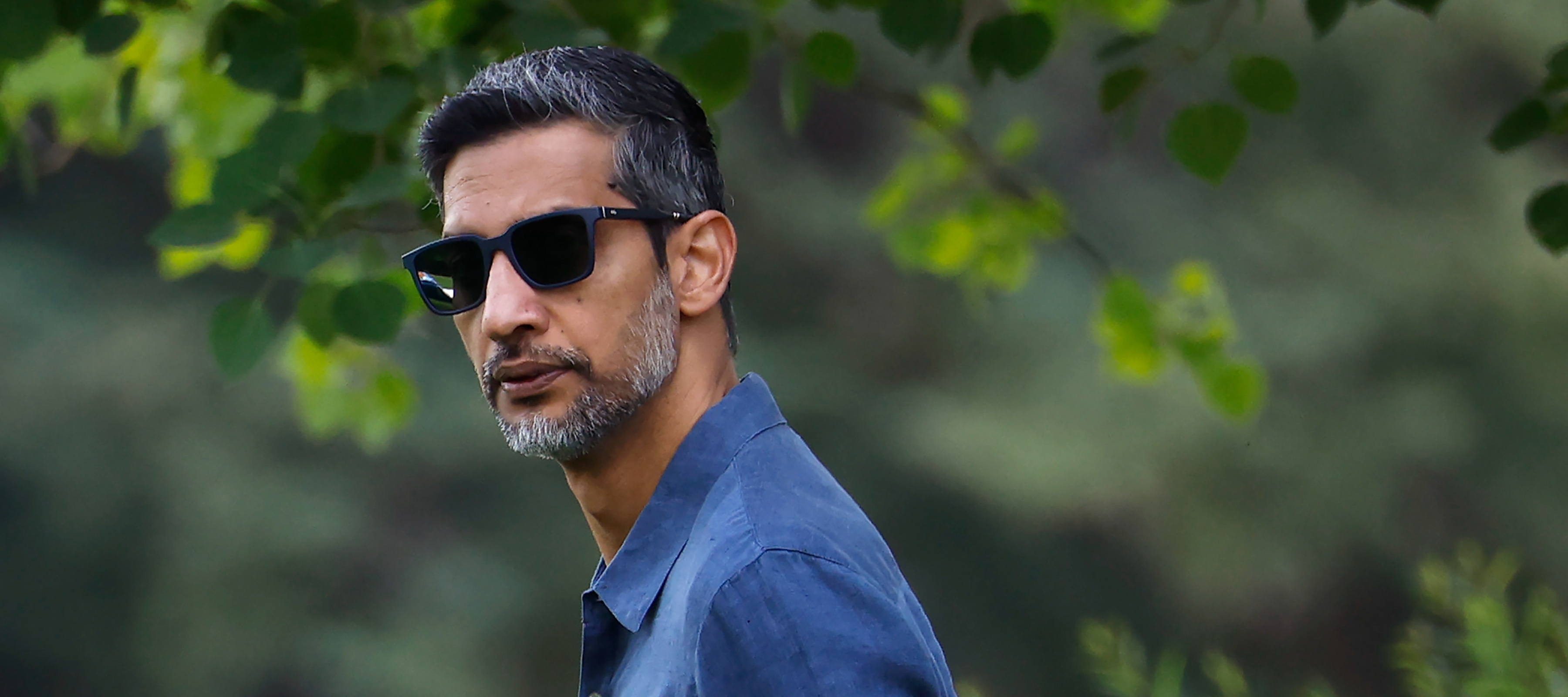 Alphabet CEO Sundar Pichai looks serious wearing sunglasses in front of some greenery