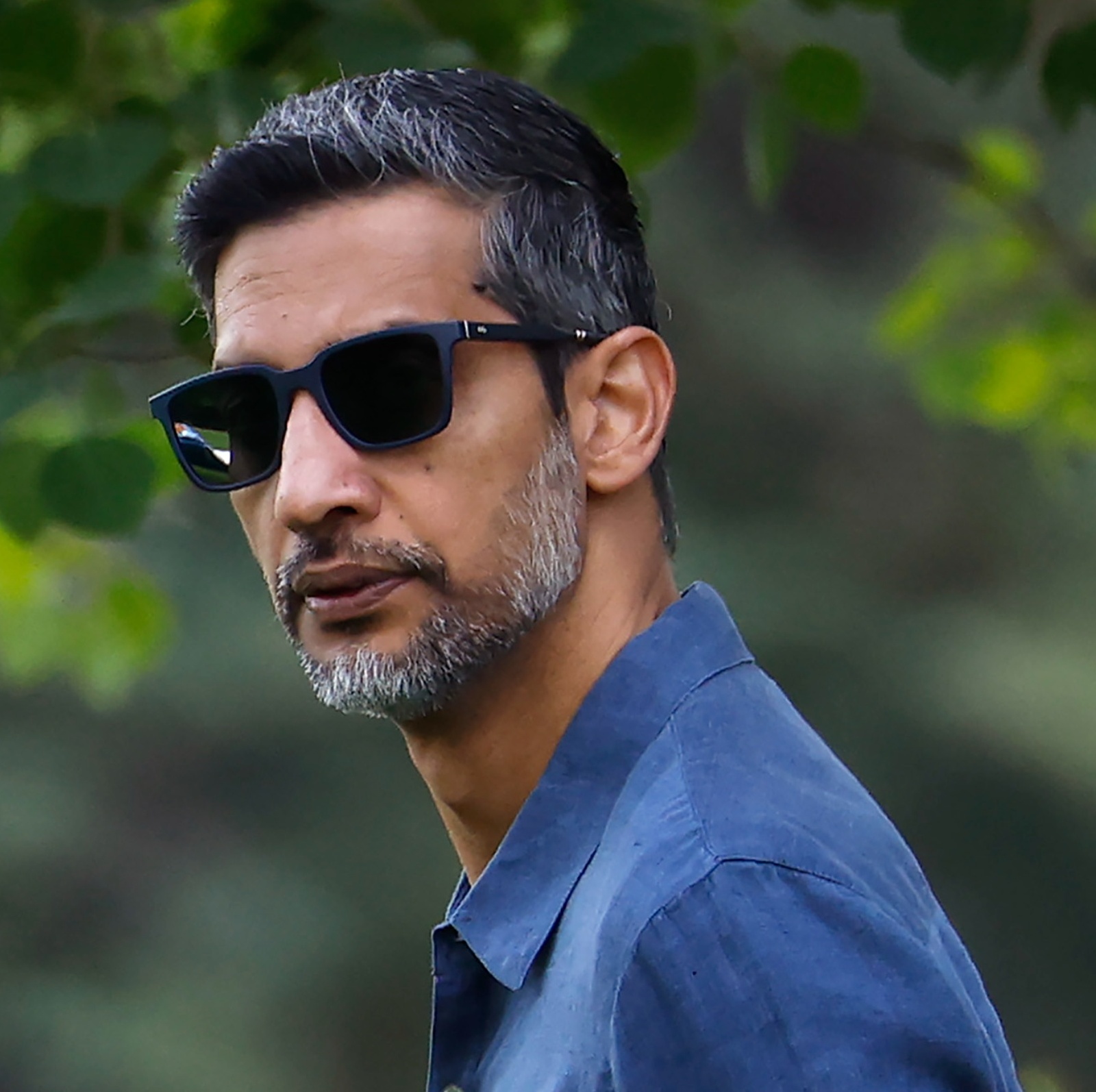 Alphabet CEO Sundar Pichai looks serious wearing sunglasses in front of some greenery