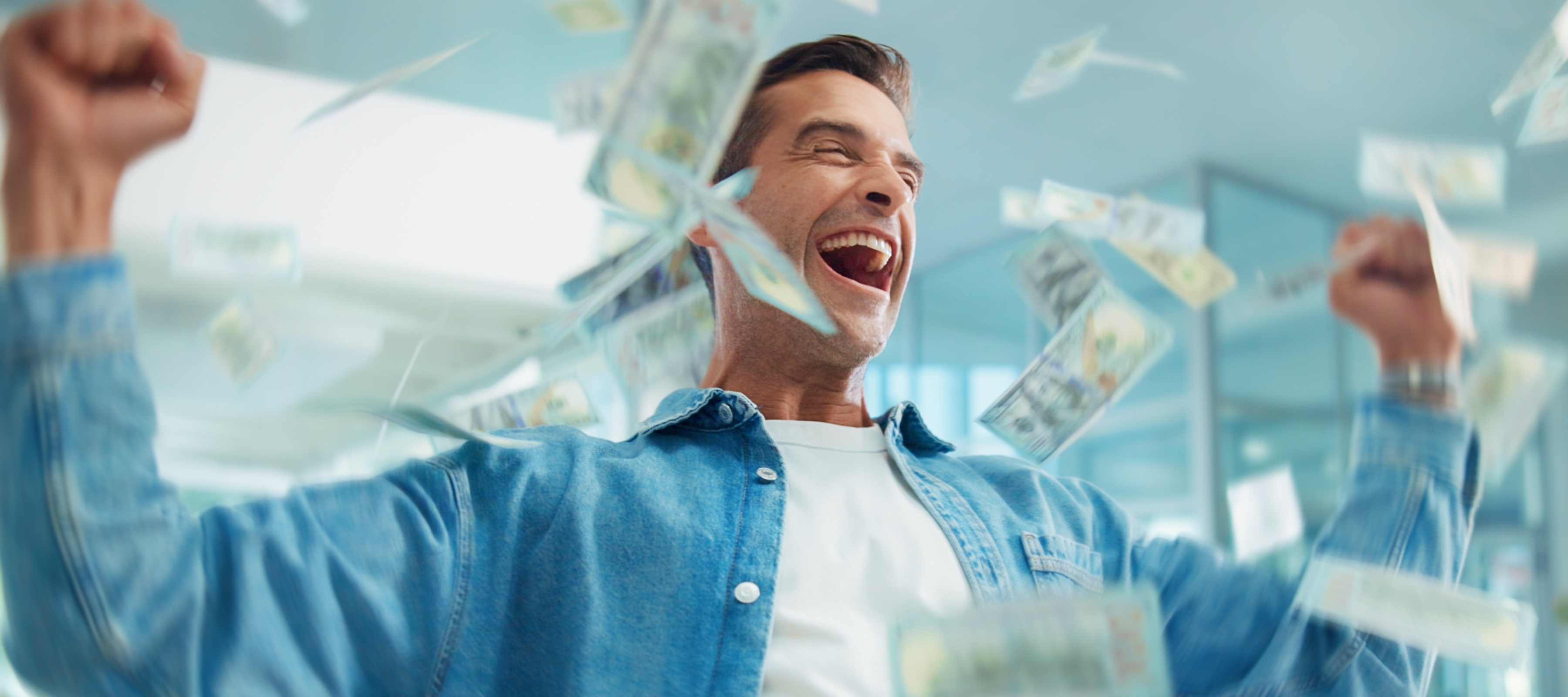 A man celebrating with his hands in the air as money flies around him