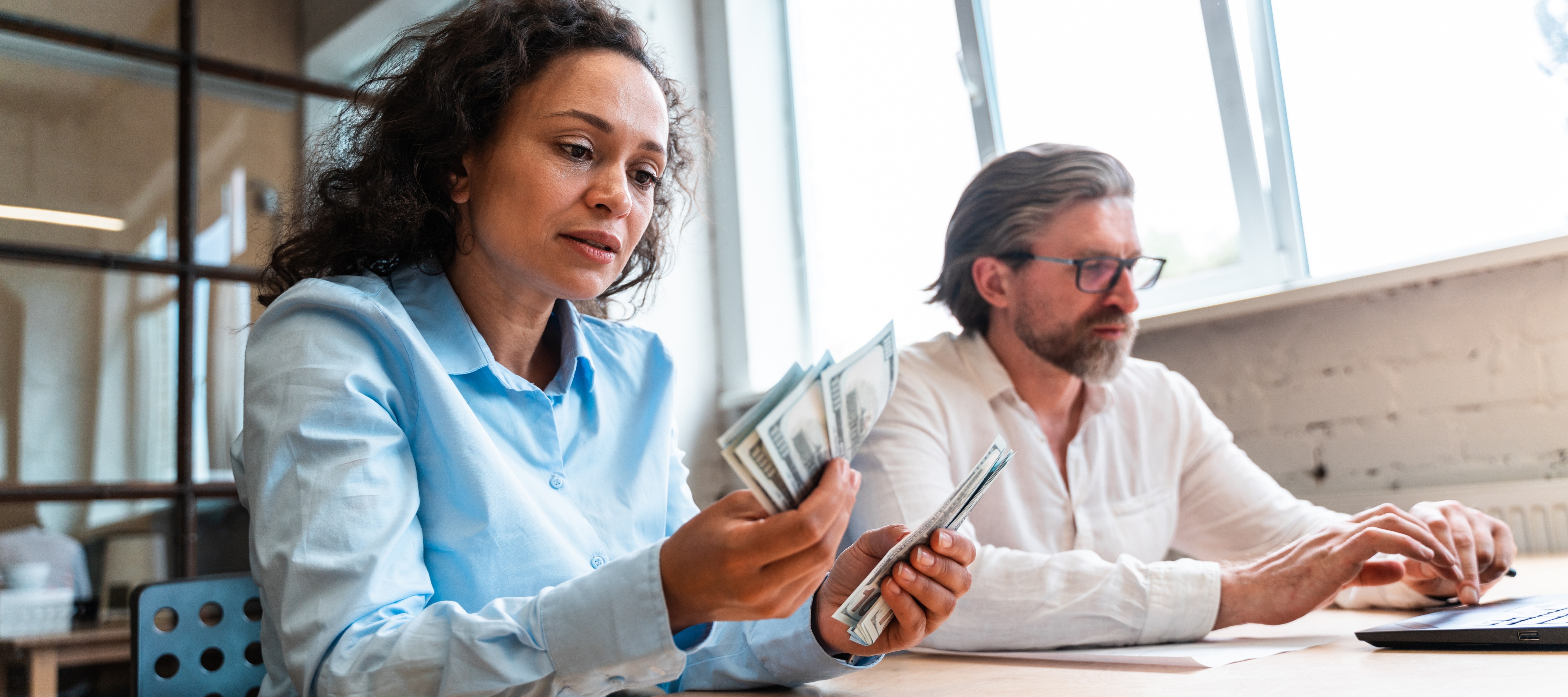 Woman counting bills next to man using laptop