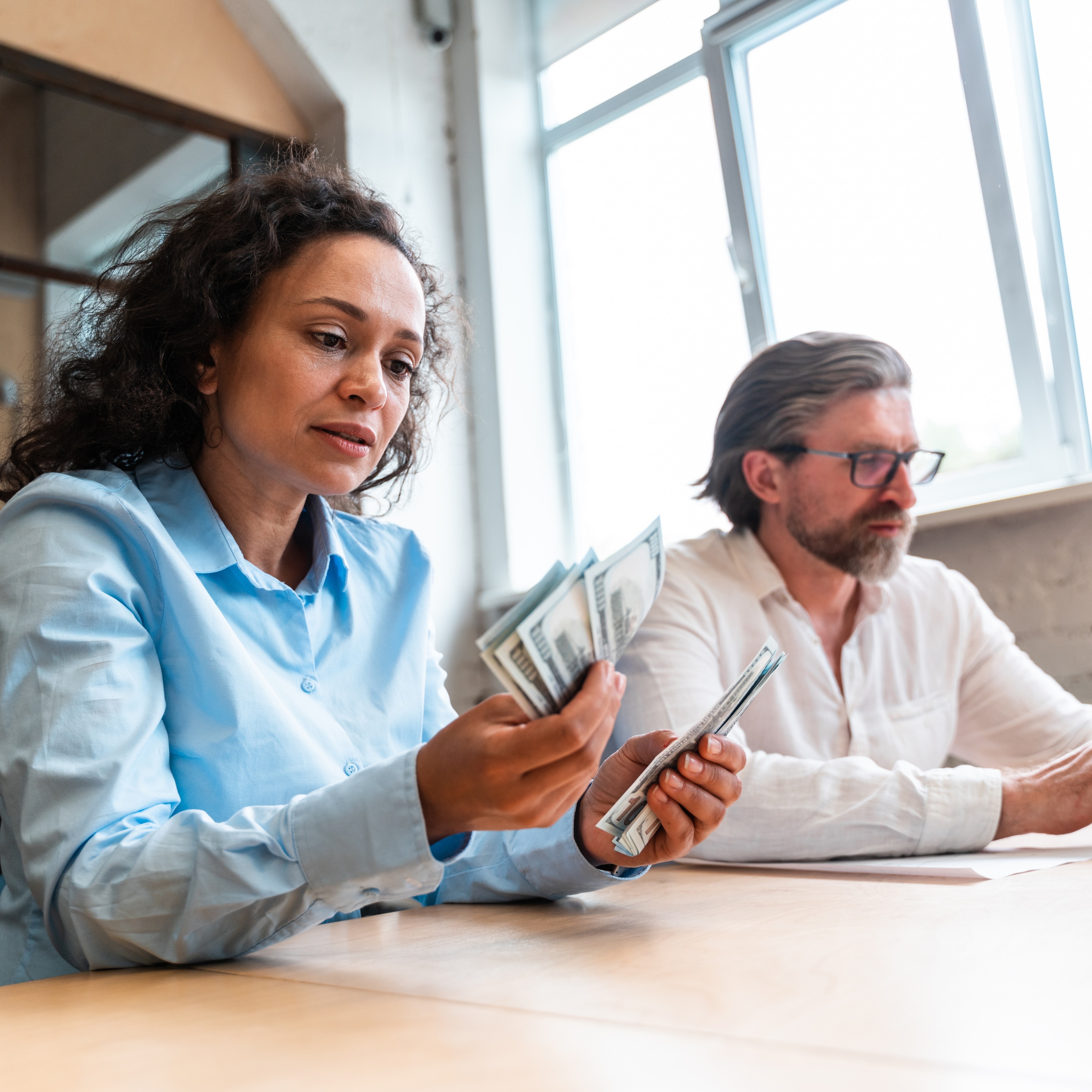 Woman counting bills next to man using laptop