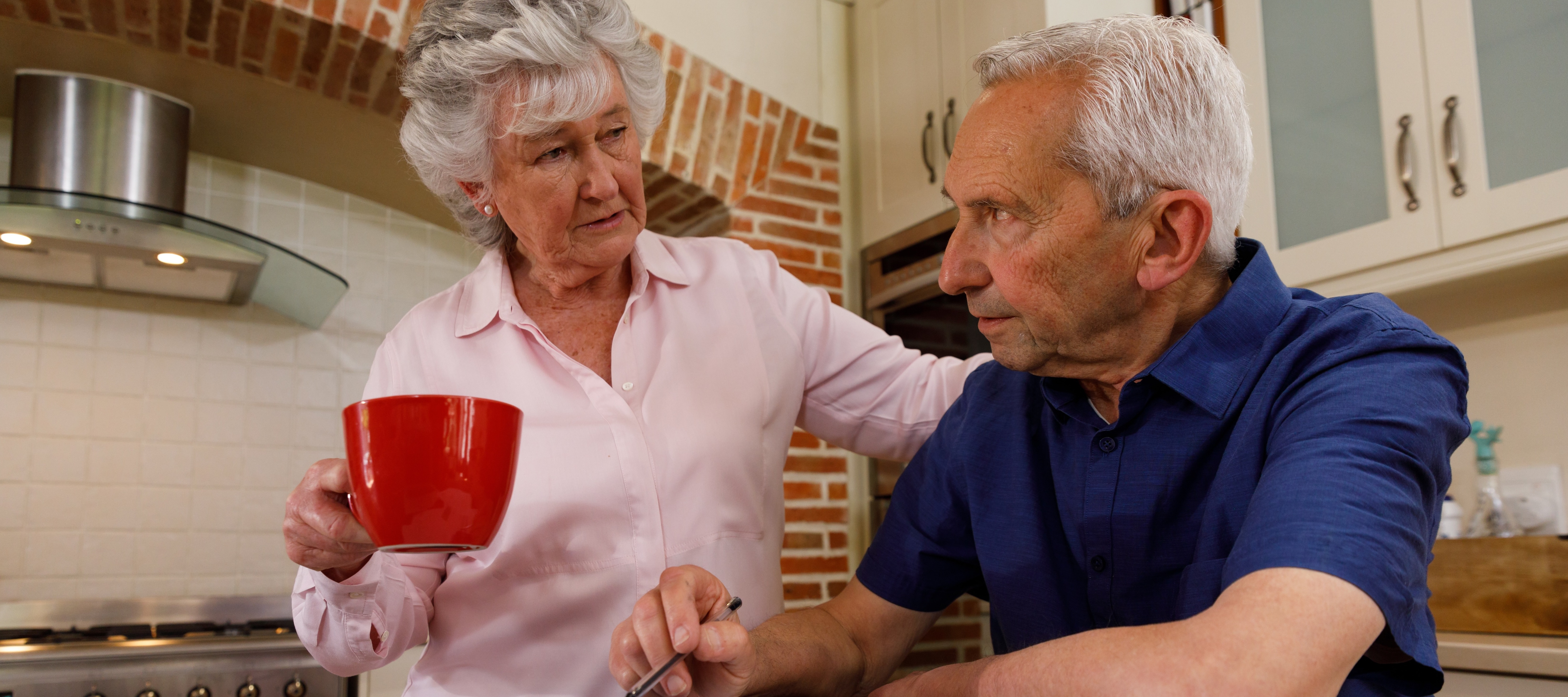 An older couple sits at a table in their home kitchen, working on finances.