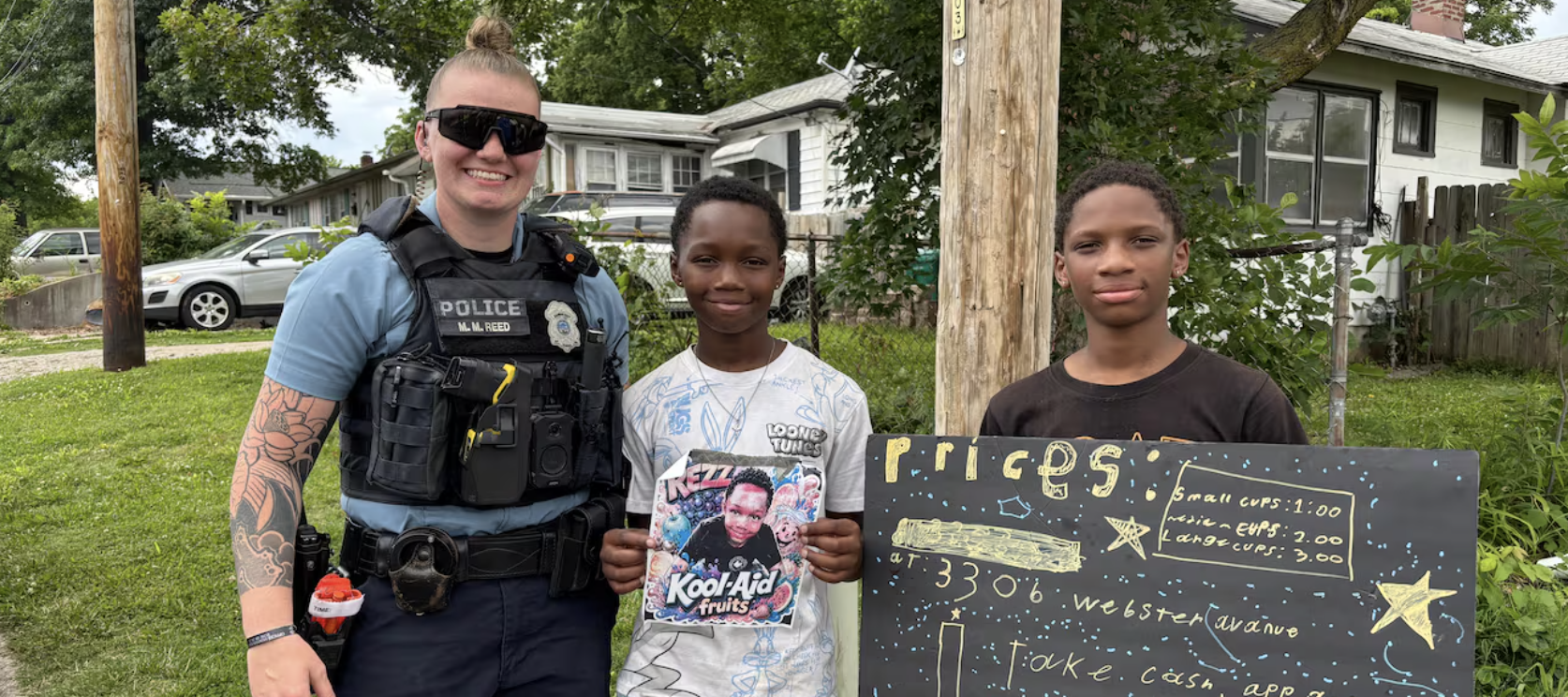 Local police officer poses for photo with two young brothers who run a lemonade stand.