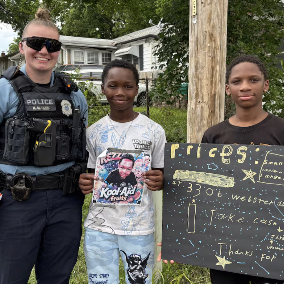 Local police officer poses for photo with two young brothers who run a lemonade stand.