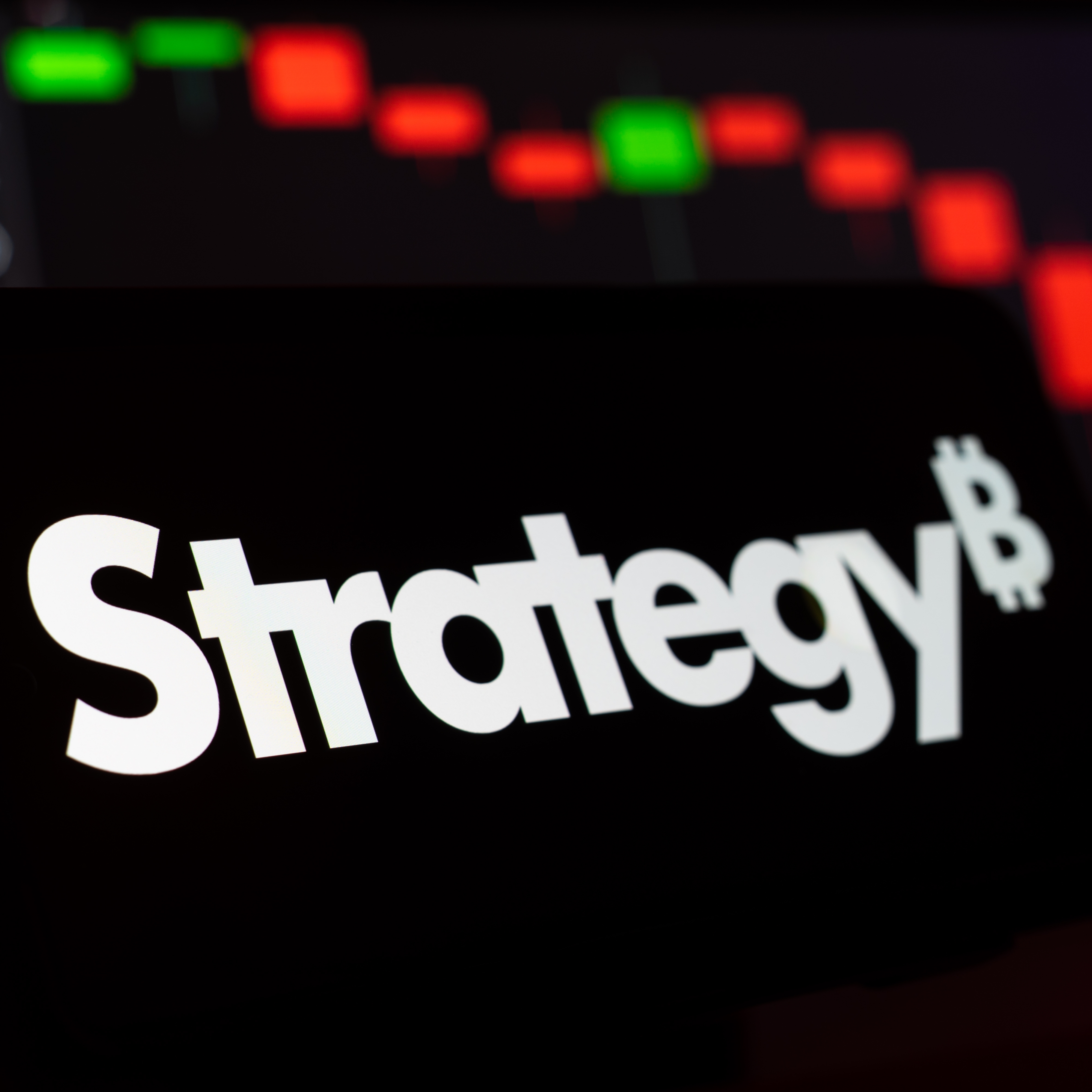 A close up of the Strategy logo on a smartphone with candlestick investing patterns in the background.