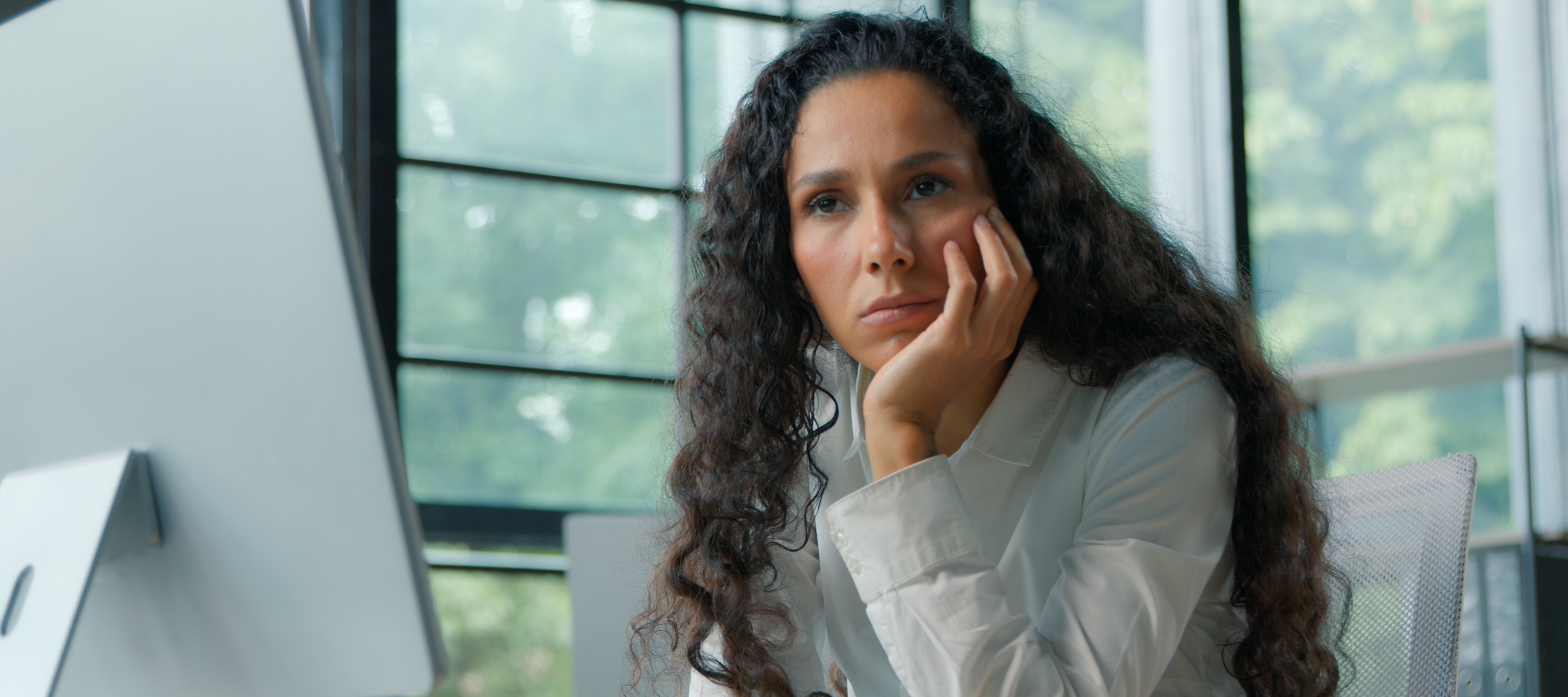 Woman working on desktop computer, zoned out and staring off into the distance, her head resting on her hand.