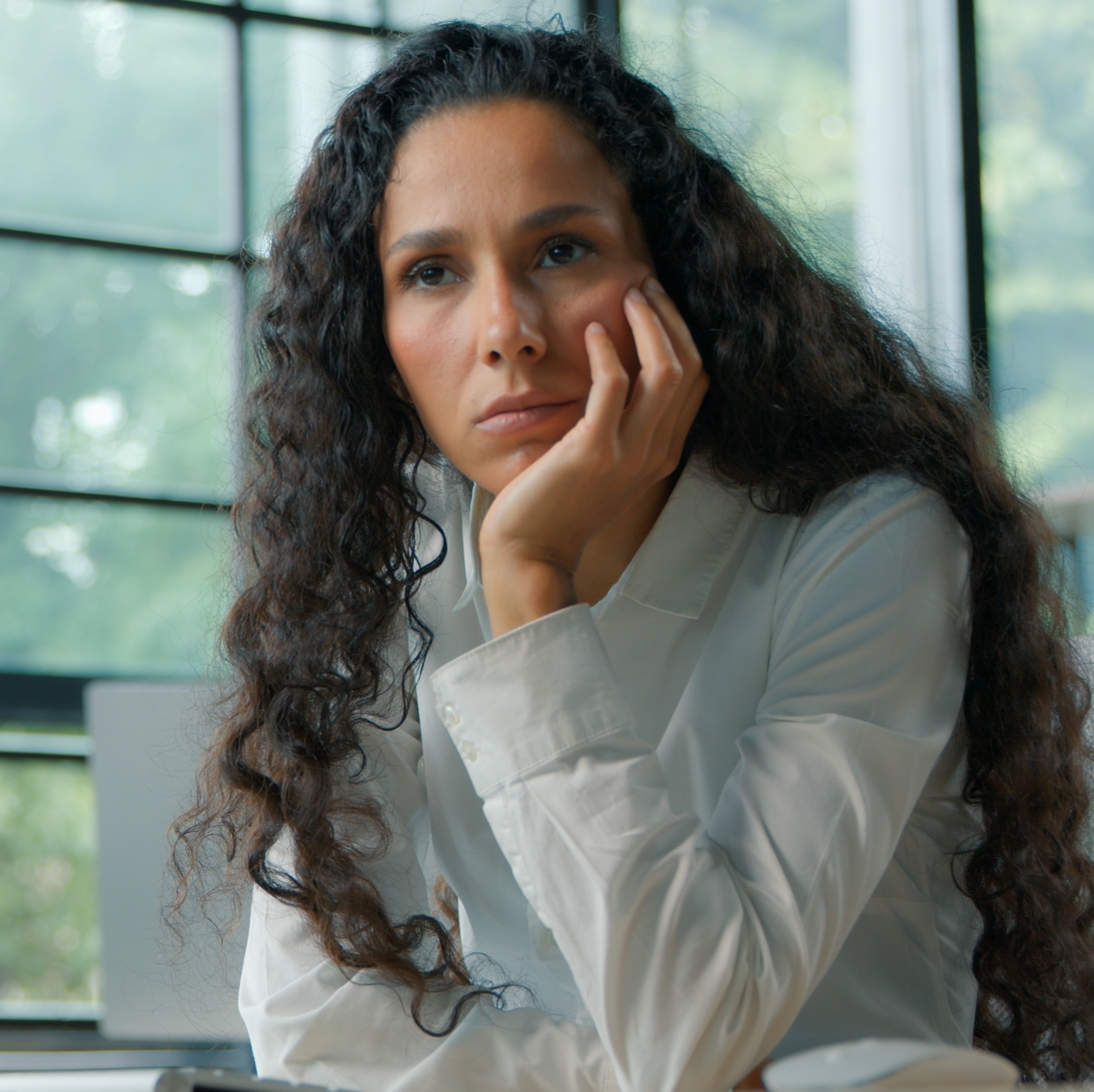 Woman working on desktop computer, zoned out and staring off into the distance, her head resting on her hand.