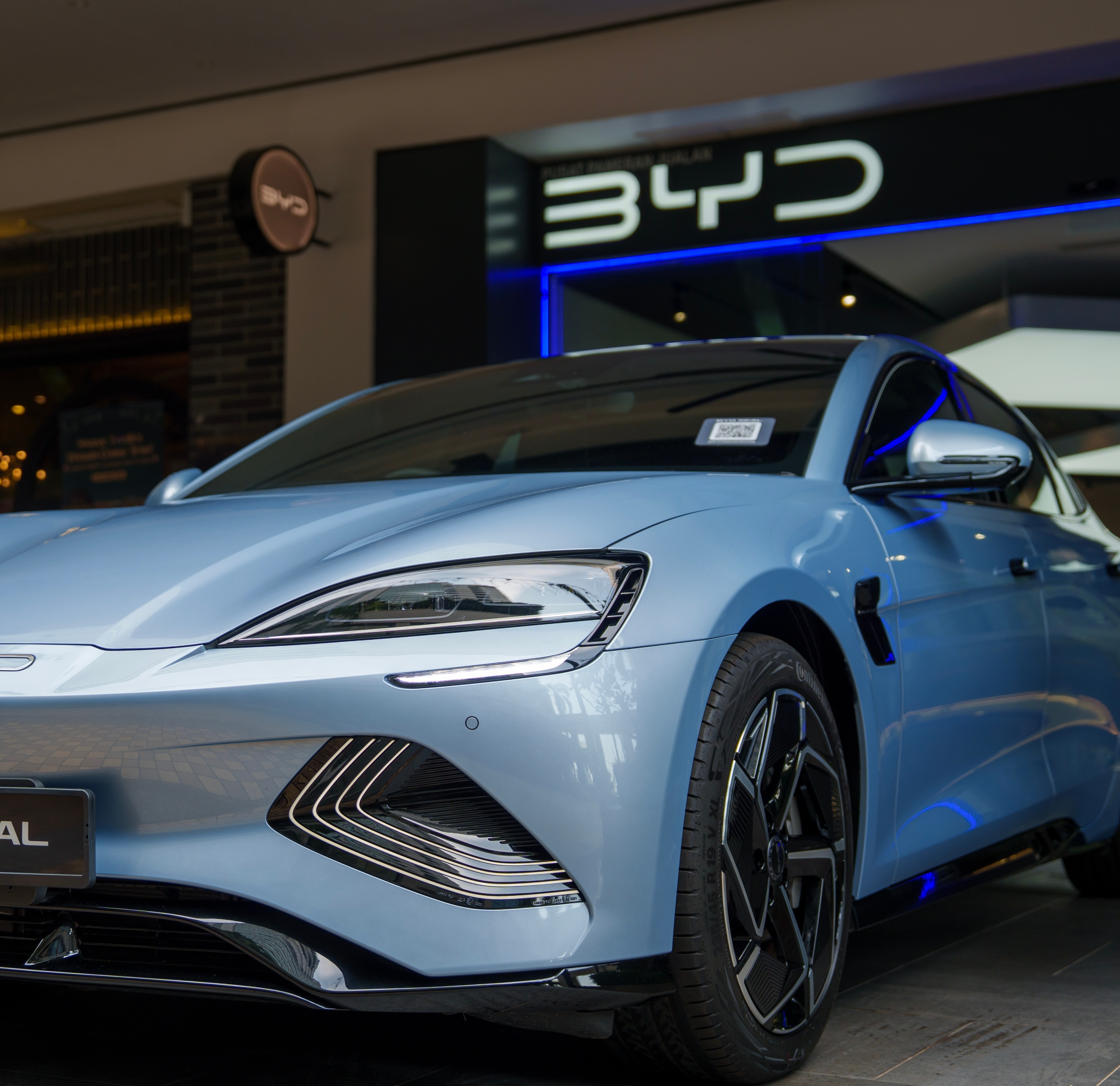 A light blue BYD Seal electric vehicle on display outside a BYD showroom