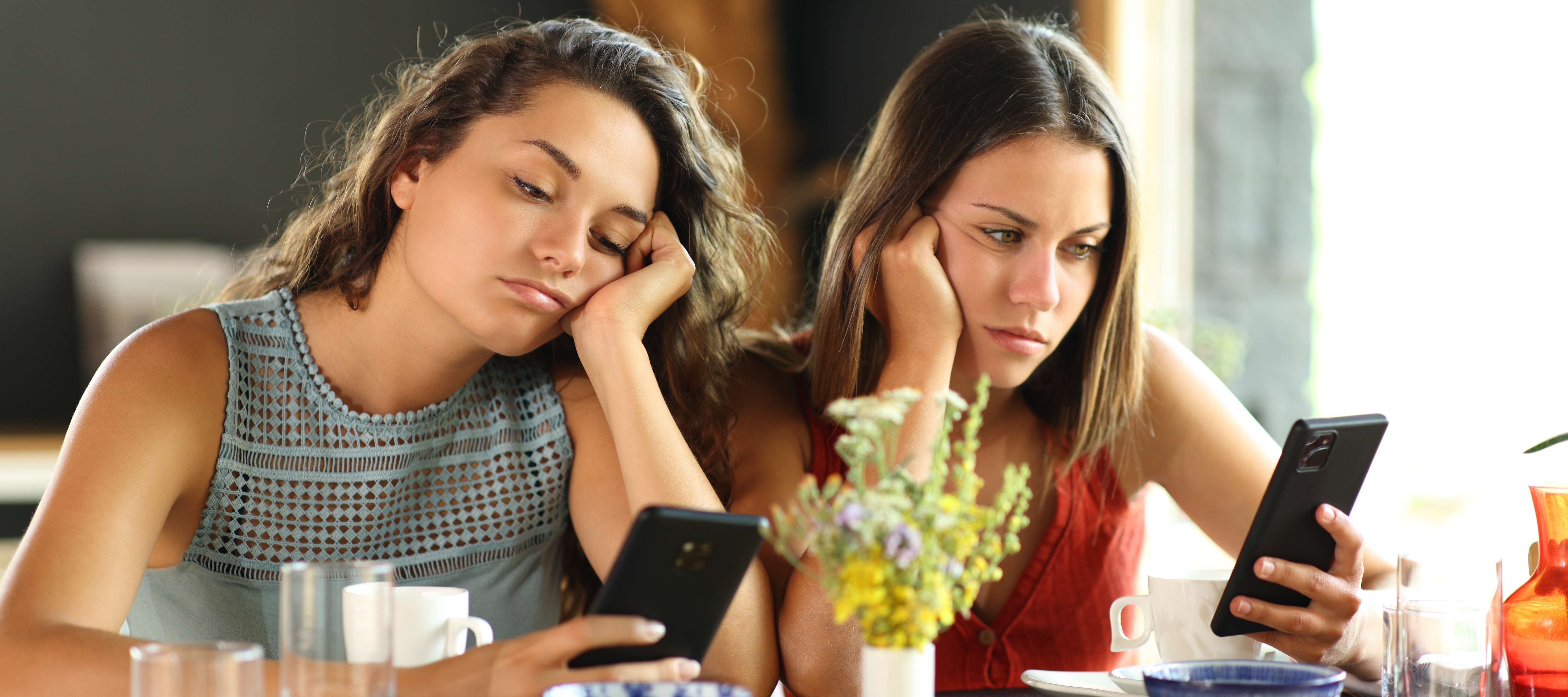 Bored women look at their phones in a restaurant.