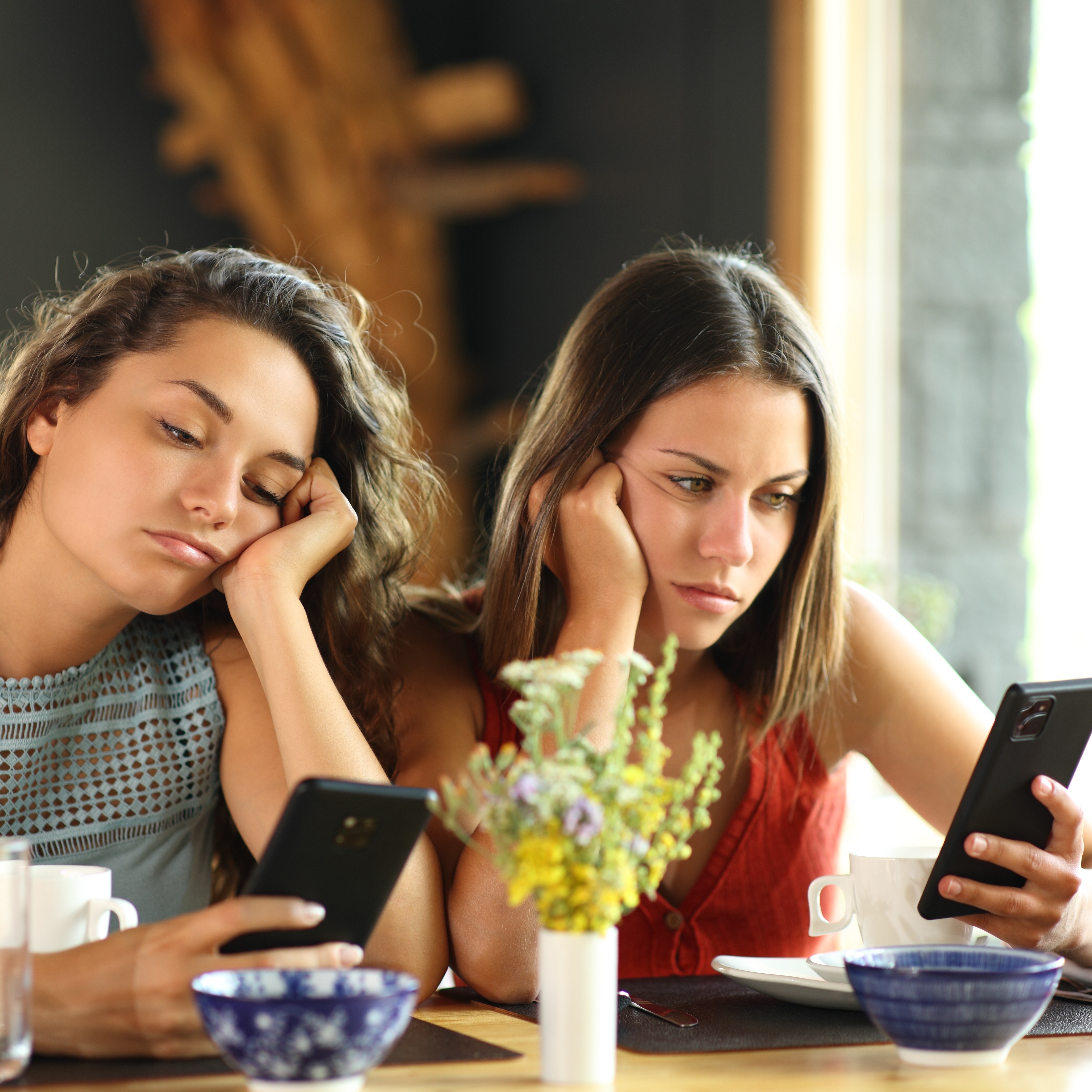 Bored women look at their phones in a restaurant.