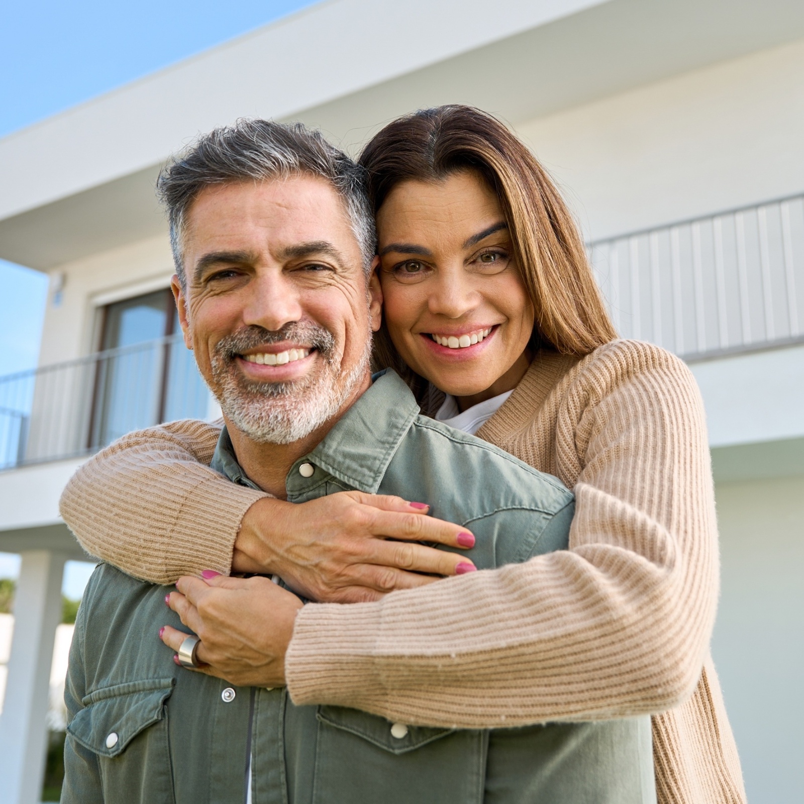 A man and woman embrace smiling at the camera in front of their newly purchased home