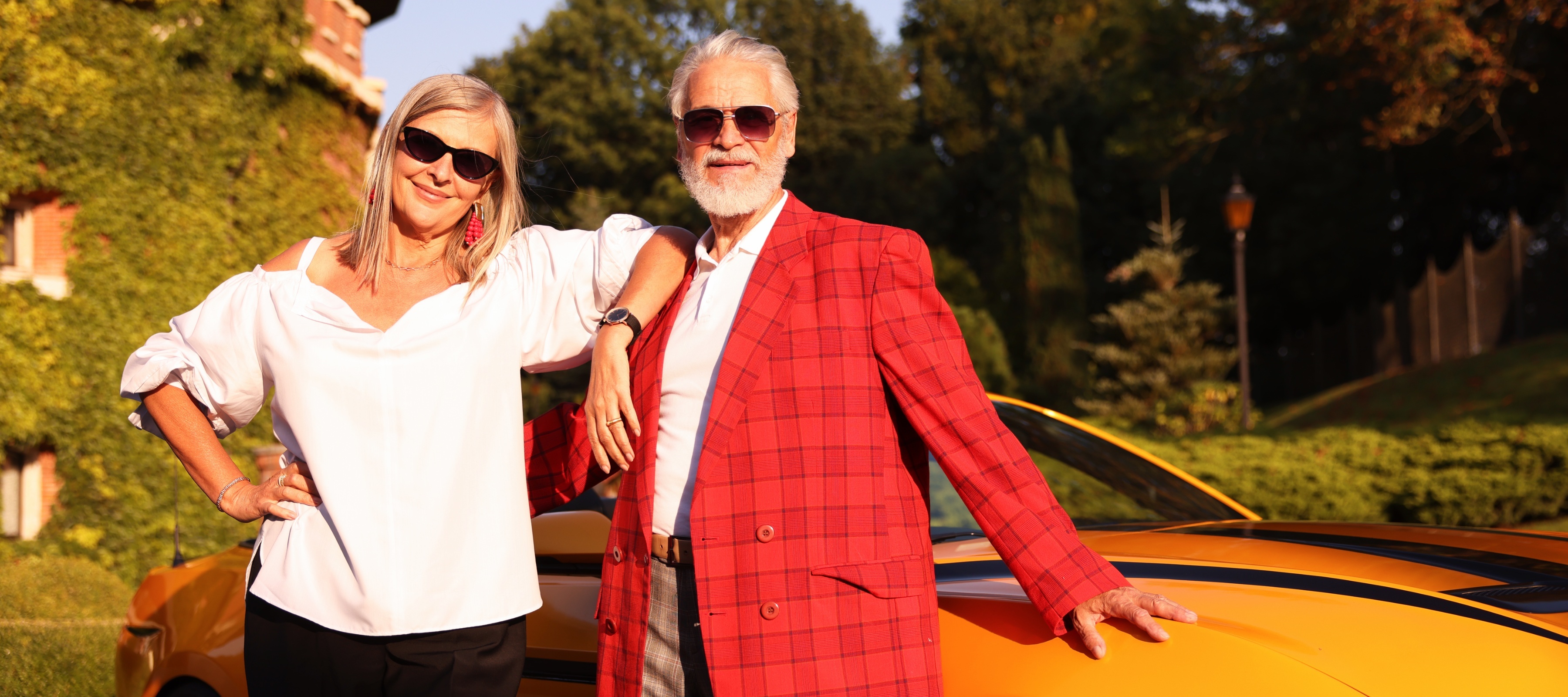 Happy older couple pose smiling outside in front of yellow sports car.