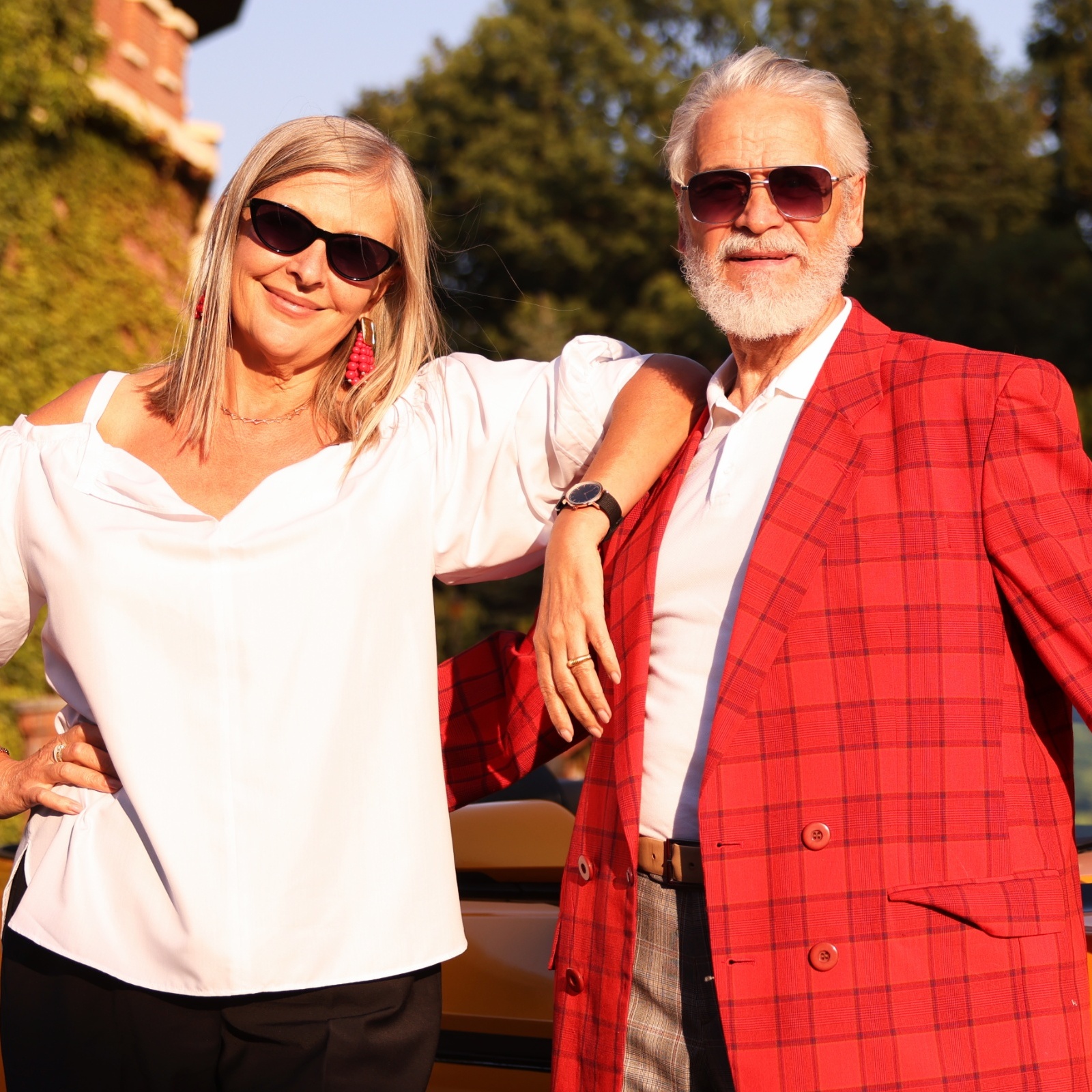 Happy older couple pose smiling outside in front of yellow sports car.