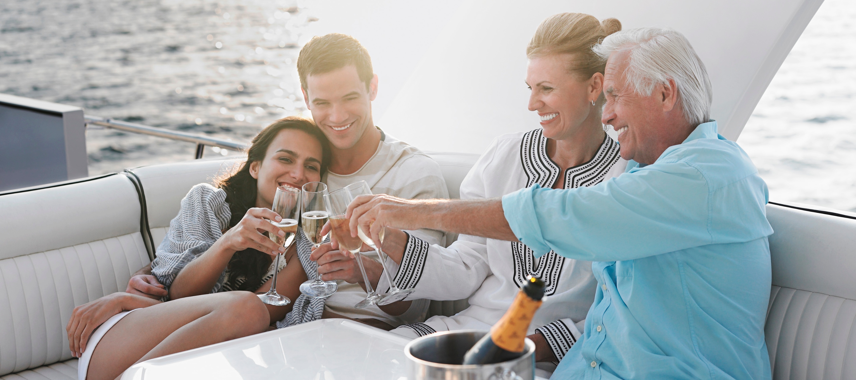 An older couple and younger couple sit together on a nice boat smiling and sharing wine