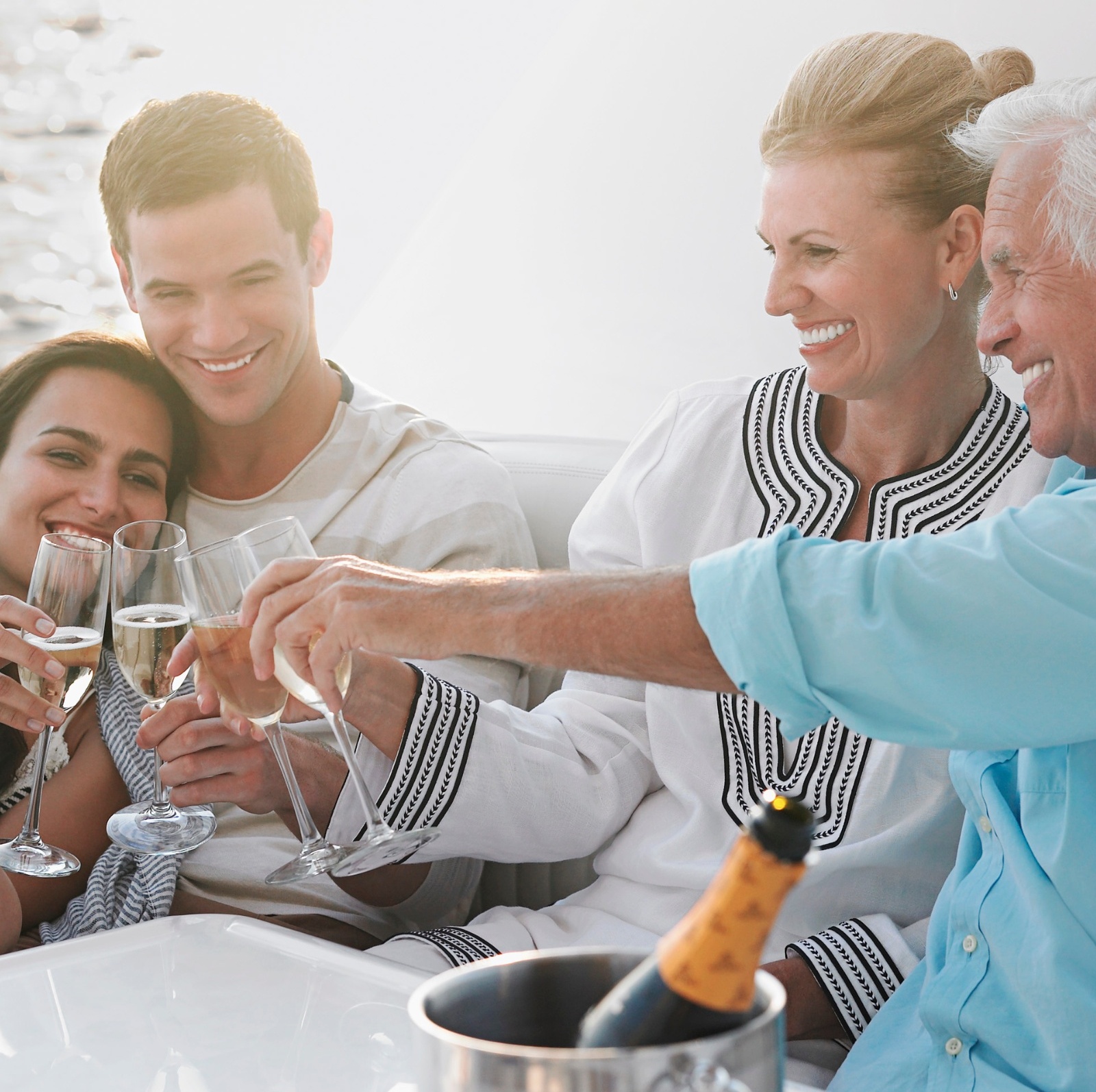 An older couple and younger couple sit together on a nice boat smiling and sharing wine