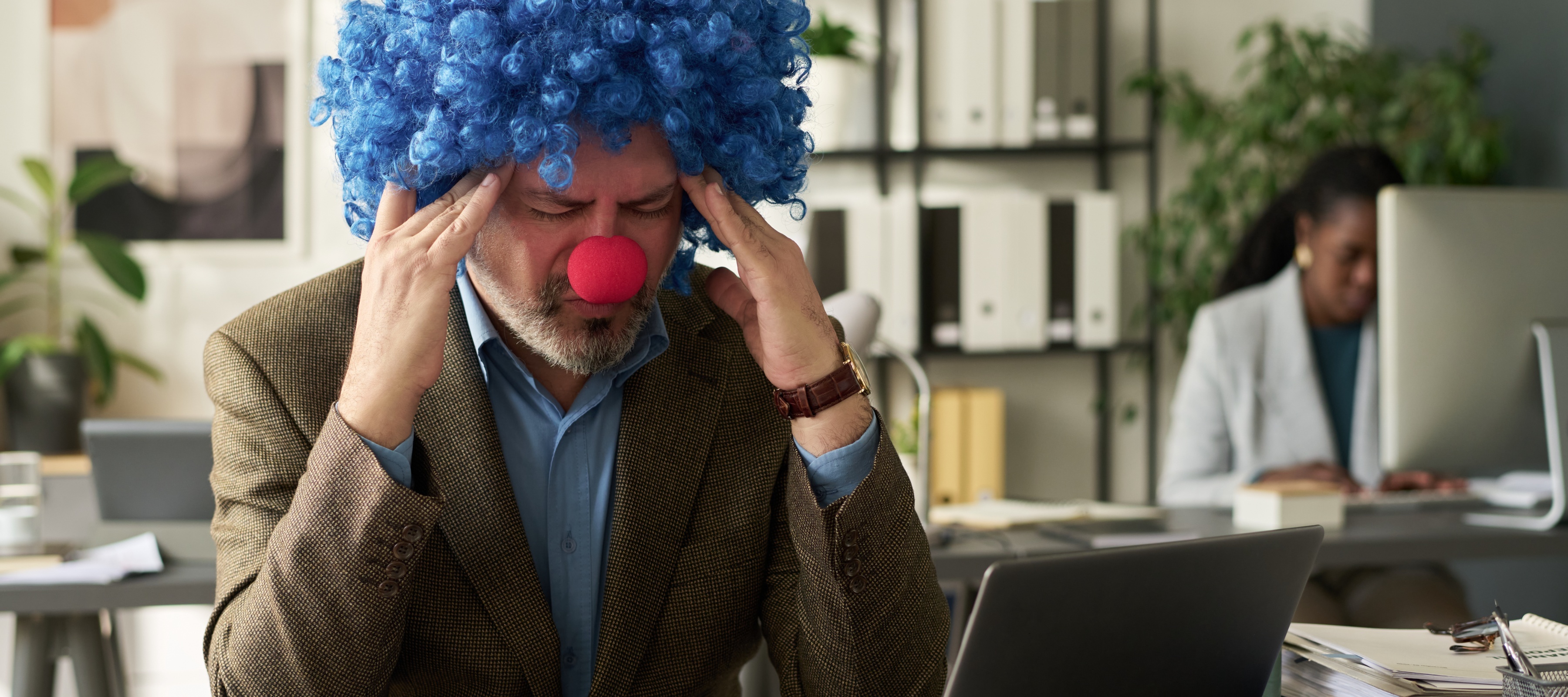 A worker who lost everything wearing a clown wig and nose at the office.