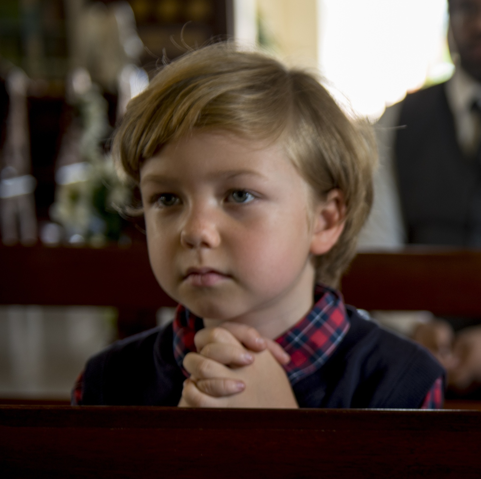 A sad-looking child and his mother clasp their hands at a pew in church