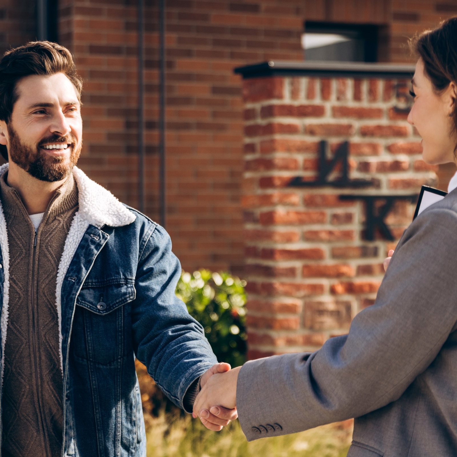 A man and woman accept keys from a real estate agent in front of a brick house