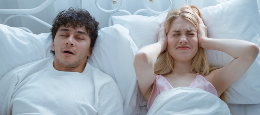 A young man snoring loudly on the bed is disturbing his wife and preventing her from sleeping.