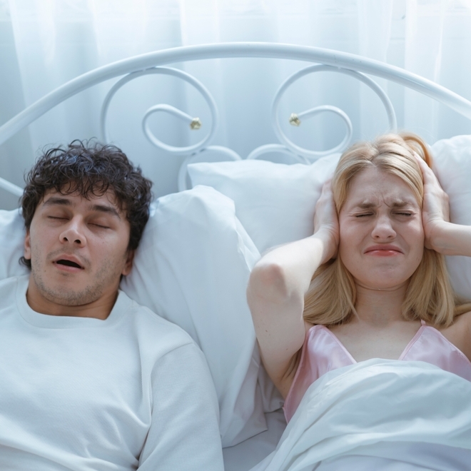 A young man snoring loudly on the bed is disturbing his wife and preventing her from sleeping.