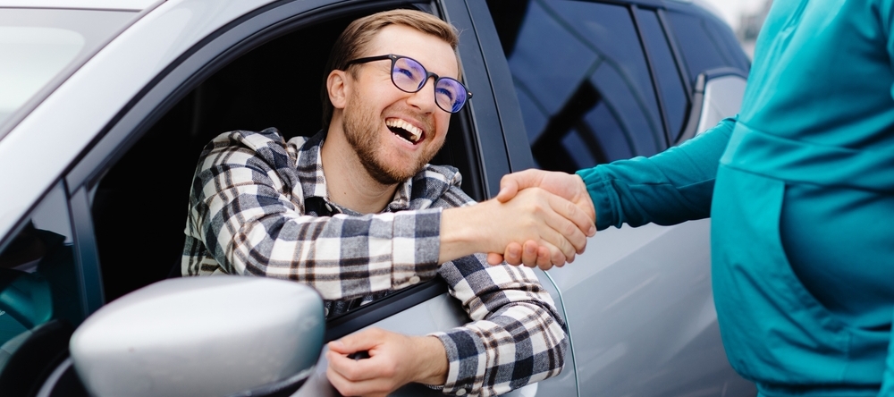 Man buying car and shaking hands with salesman against blurred auto, closeup.
