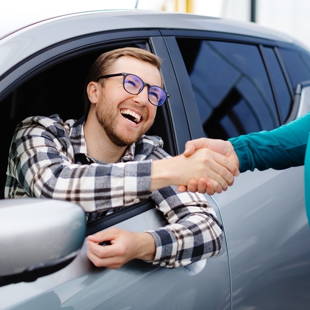 Man buying car and shaking hands with salesman against blurred auto, closeup.