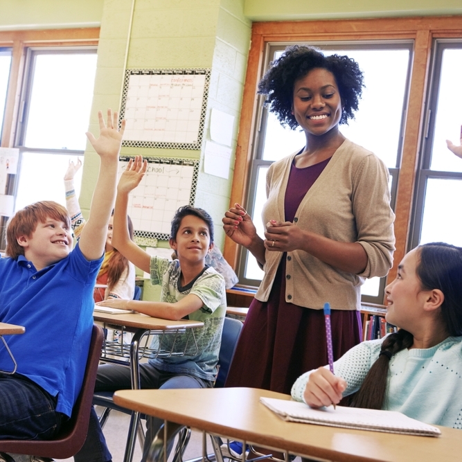 A photo of a teacher in a classroom full of students raising their hands