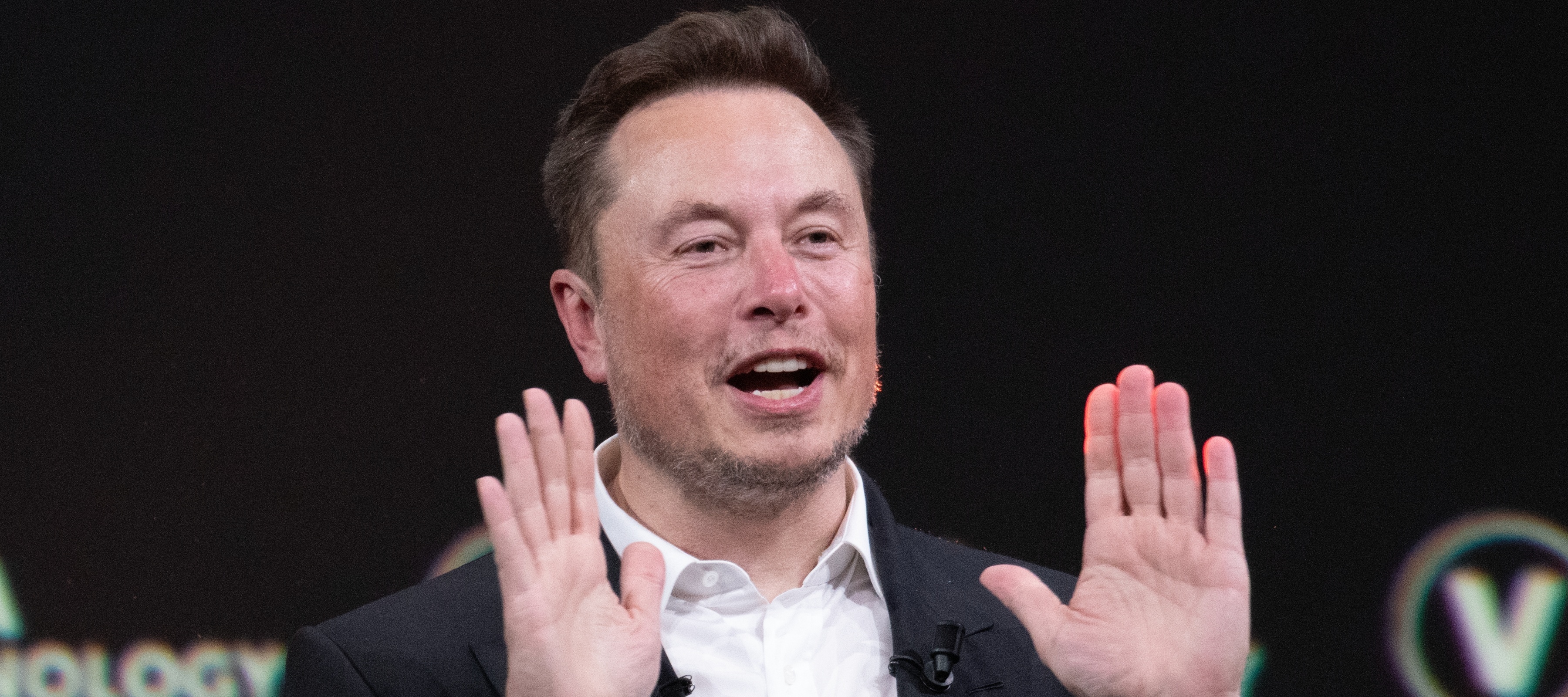 Elon Musk holds up both hands in the air