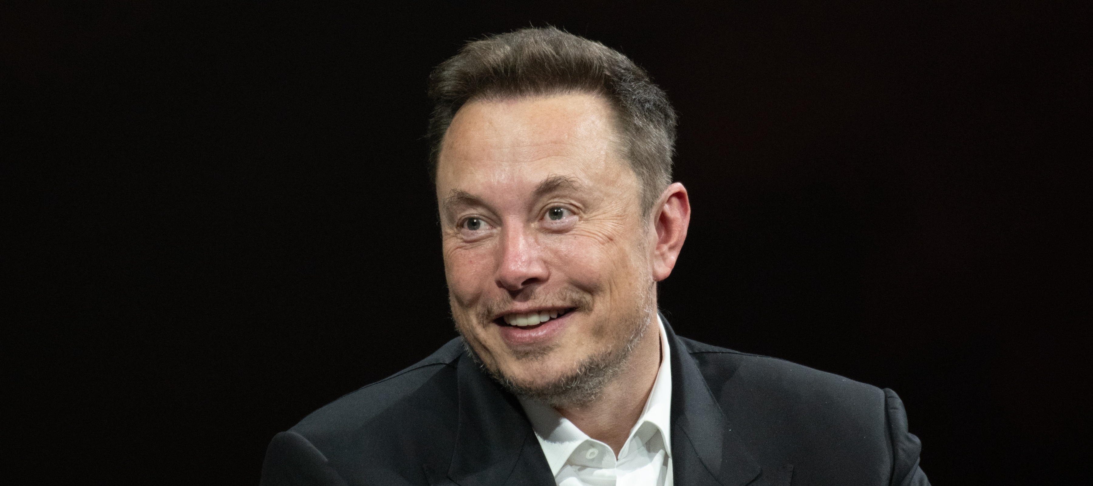 Elon Musk smiling big with his eyes wide