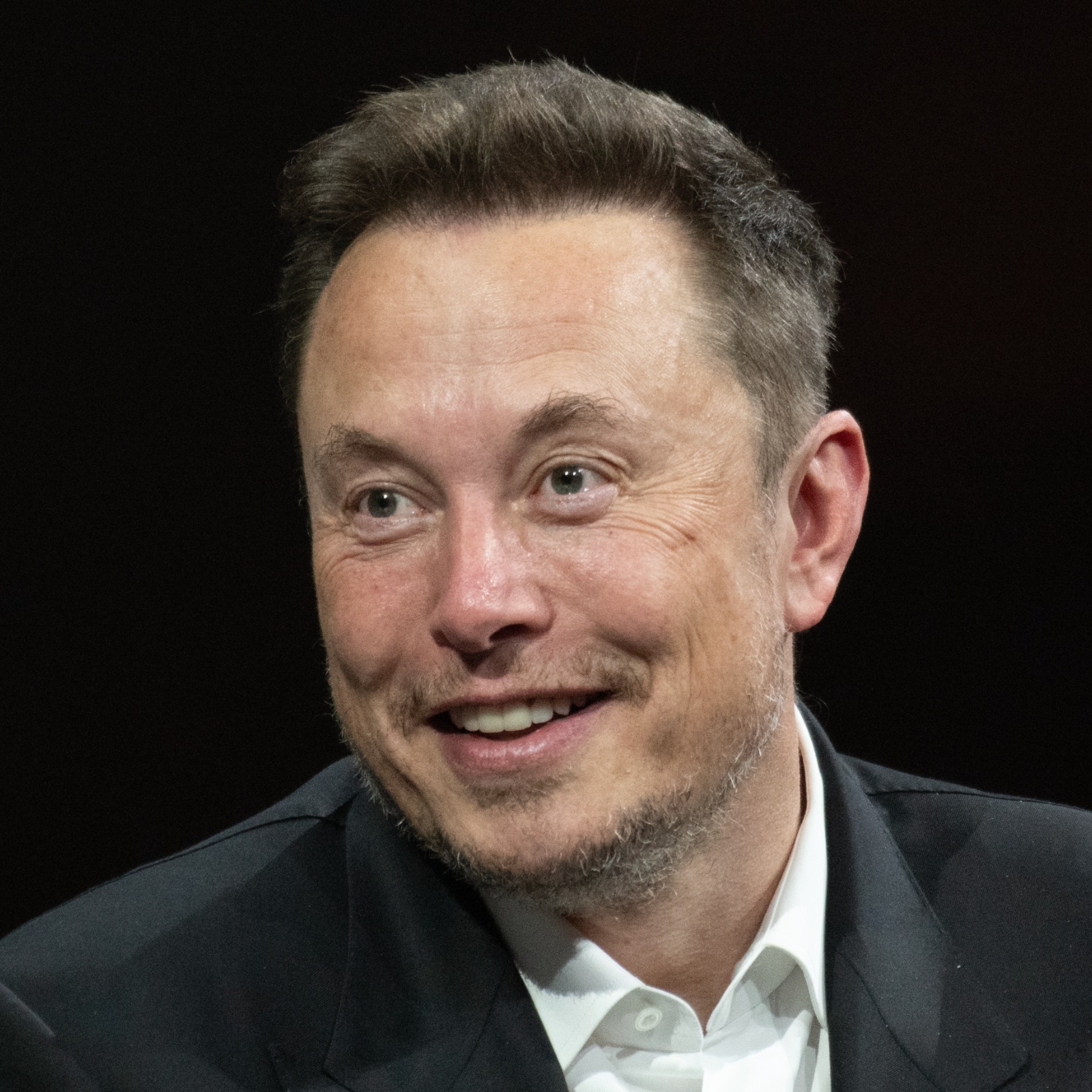 Elon Musk smiling big with his eyes wide