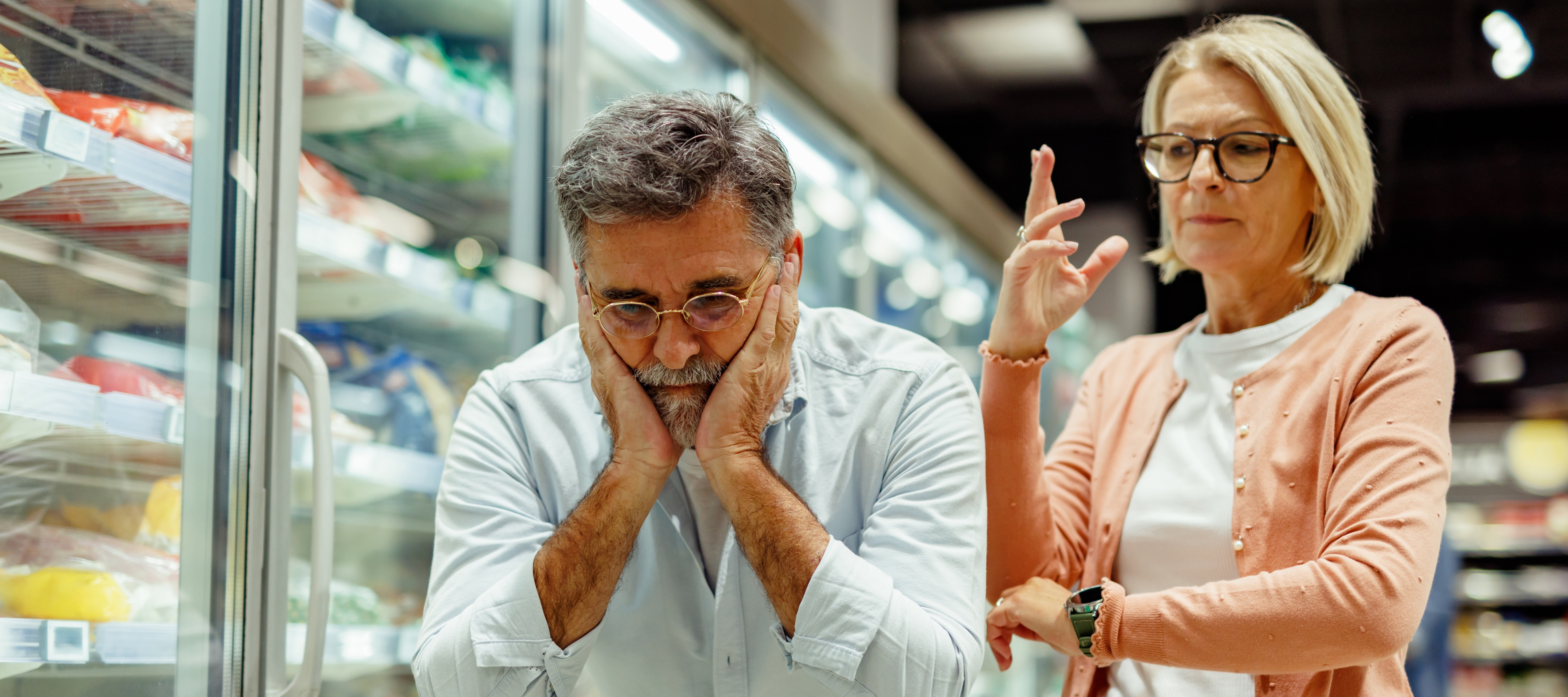 Elderly couple argues while grocery shopping, showing stress and conflict in their relationship.