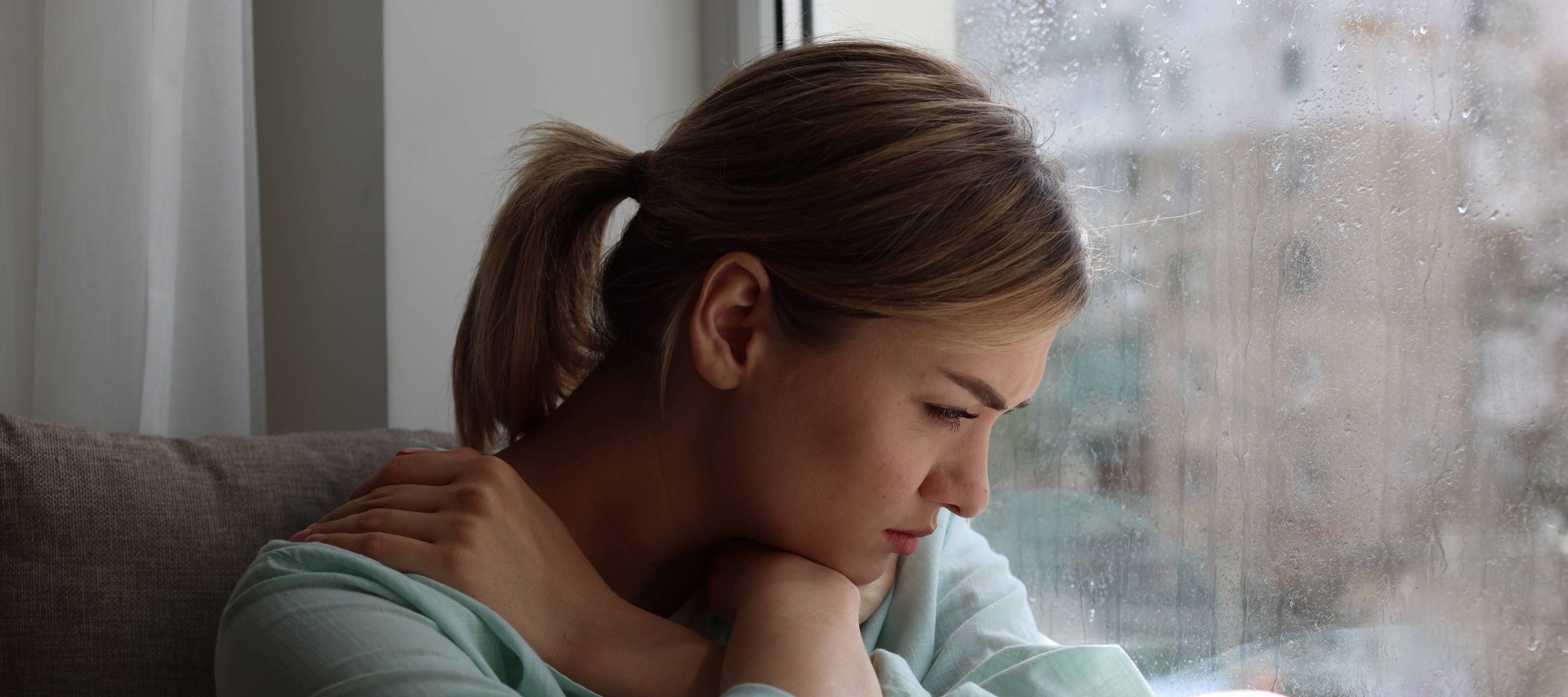 A sad-looking woman stares out her rainy window