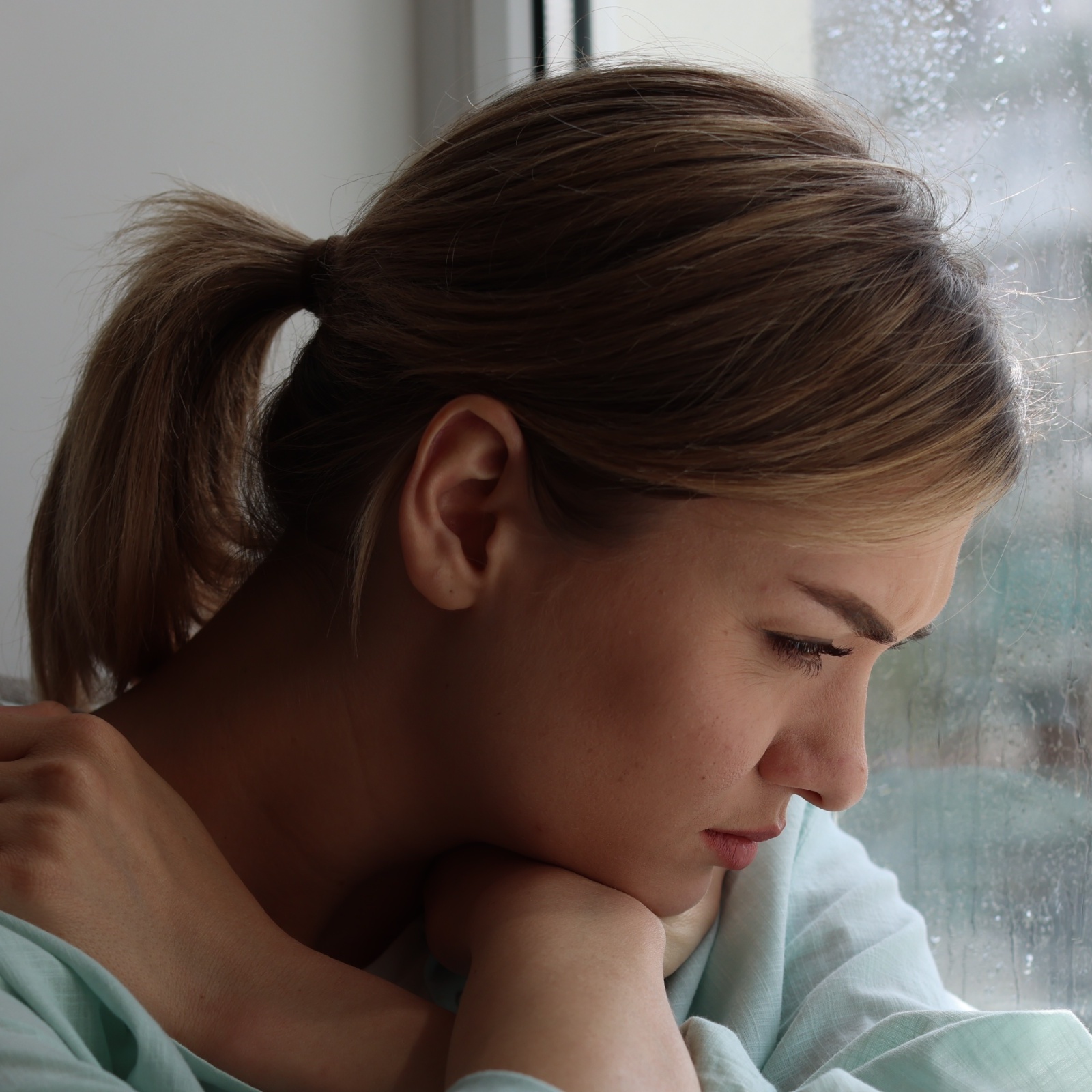 A sad-looking woman stares out her rainy window