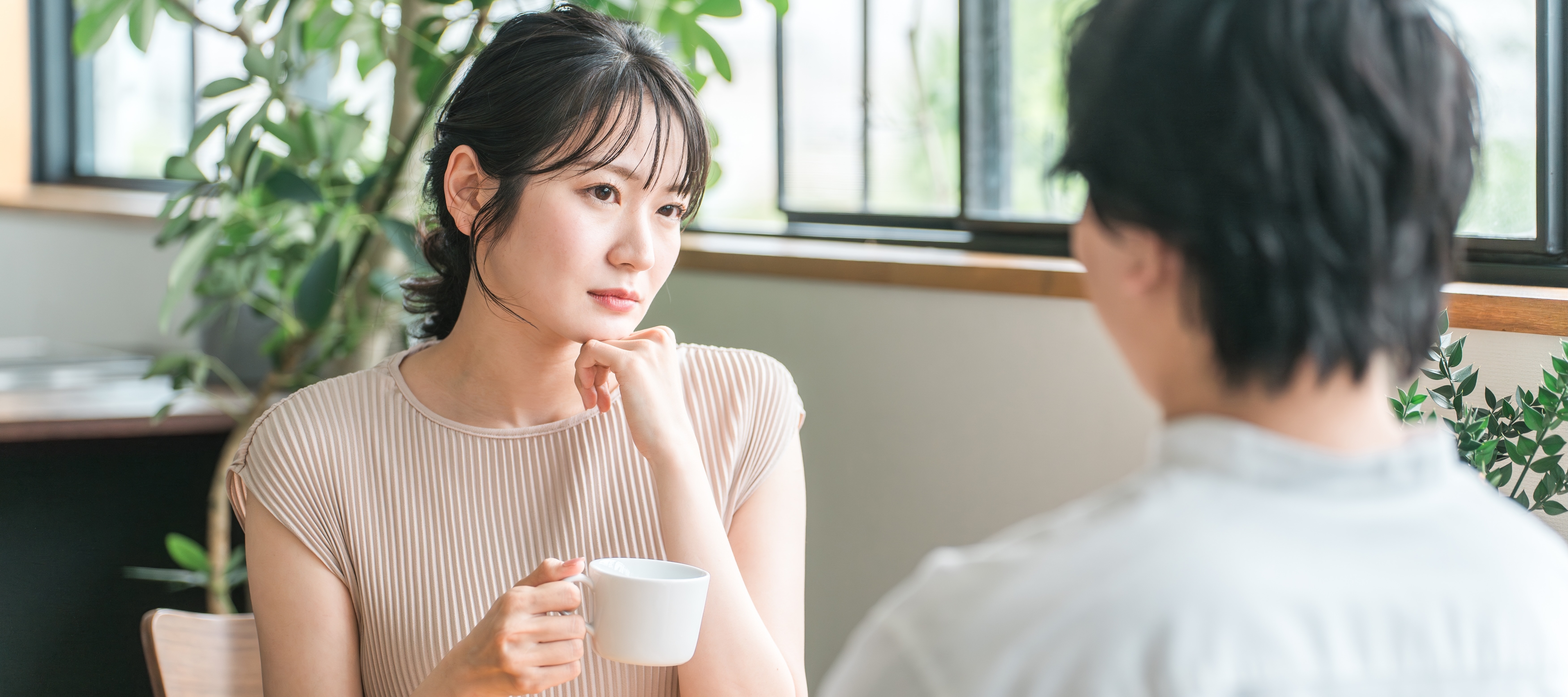 A view of a man and a woman on a date in a coffee shop from over the man's shoulder; the woman looks tentative or nervous.