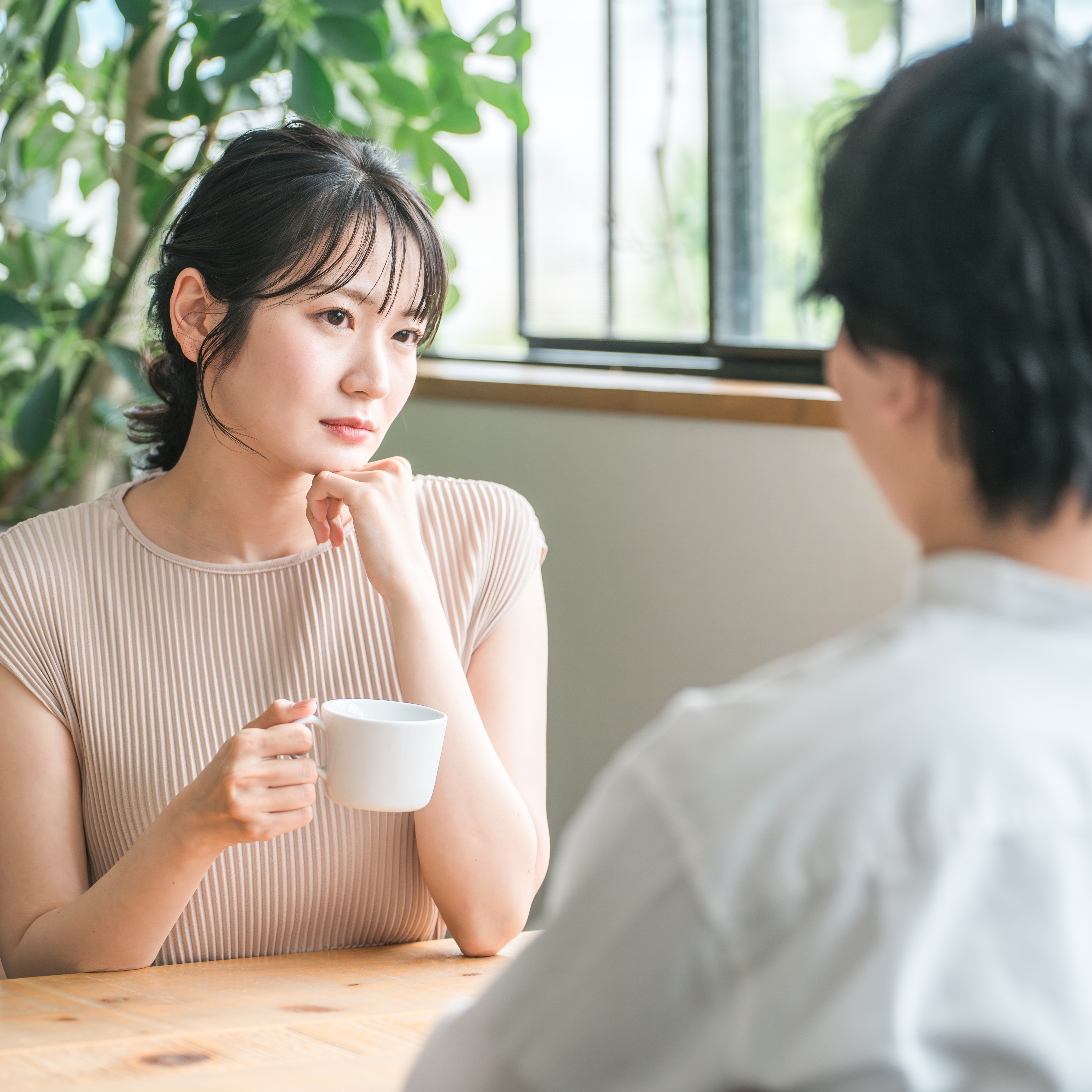 A view of a man and a woman on a date in a coffee shop from over the man's shoulder; the woman looks tentative or nervous.