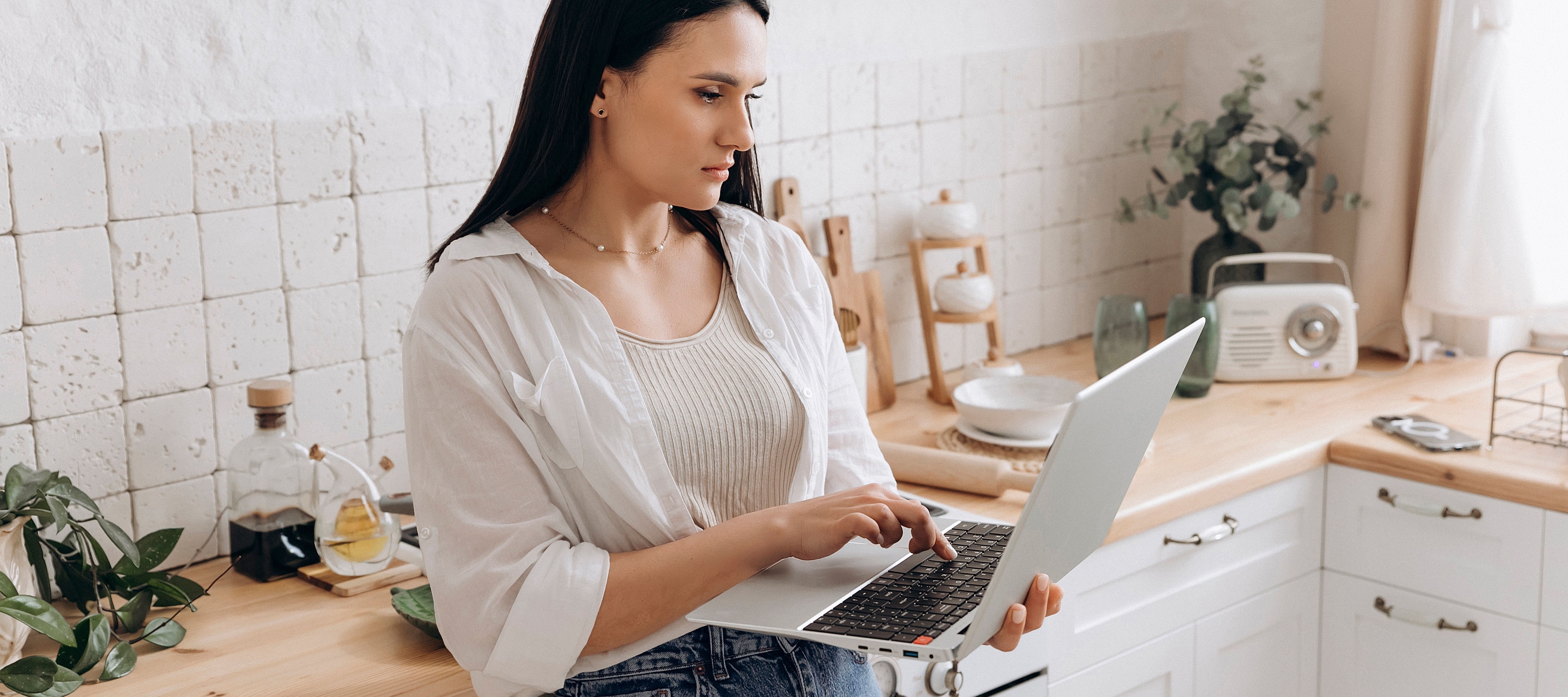 A woman works on her computer while standing in the kitchen.