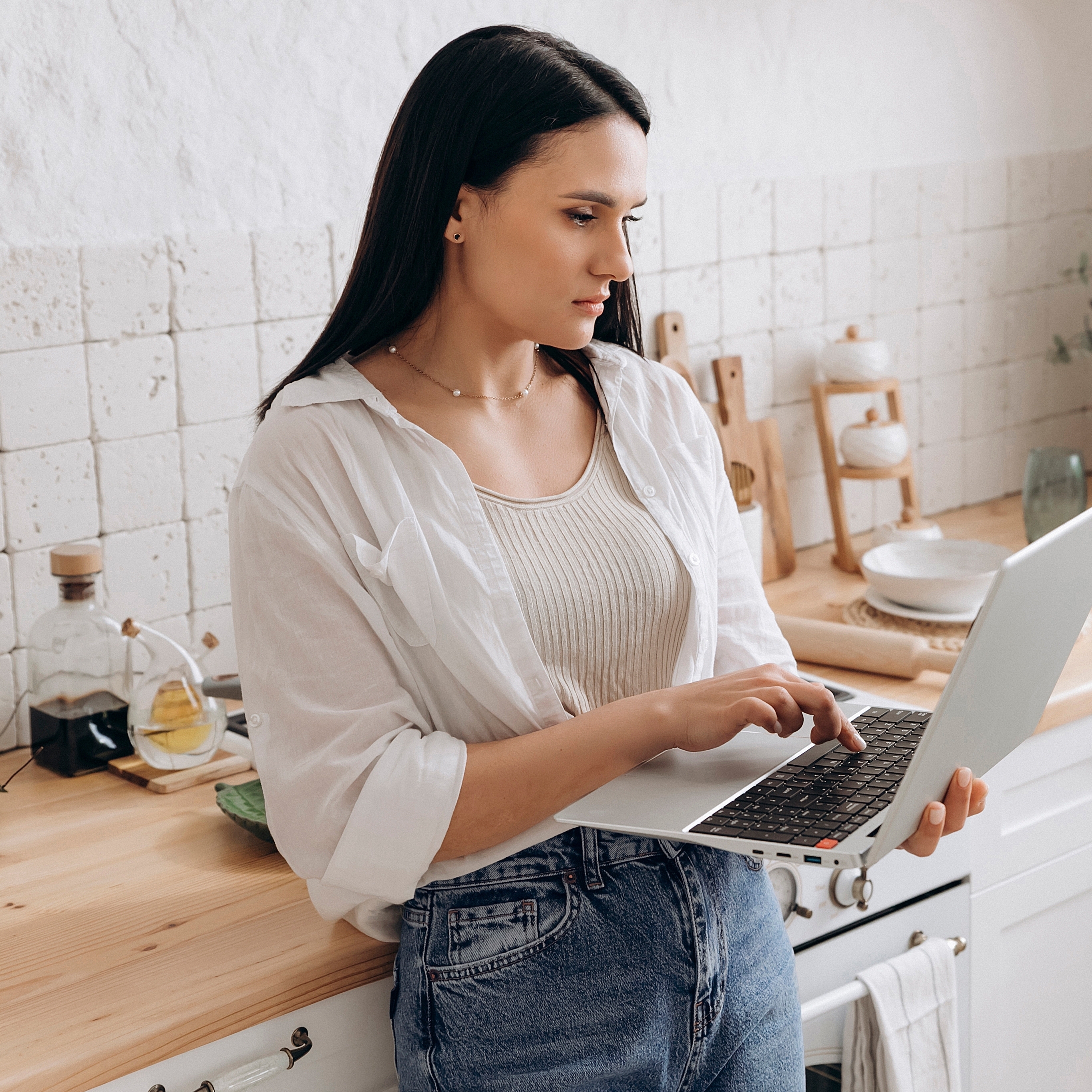 A woman works on her computer while standing in the kitchen.
