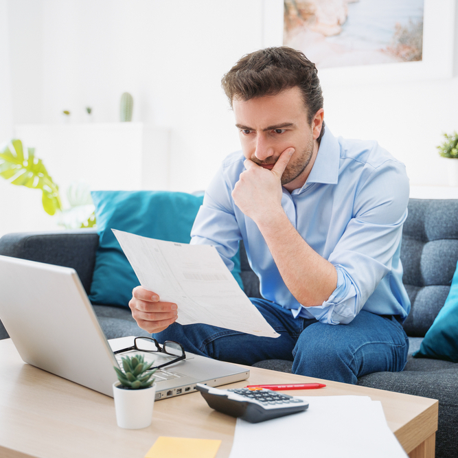 Man looks at a sheet of paper, wondering if he should pay off his debts.