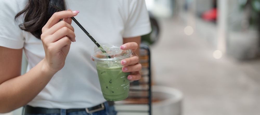 A photo of a woman drinking an iced matcha