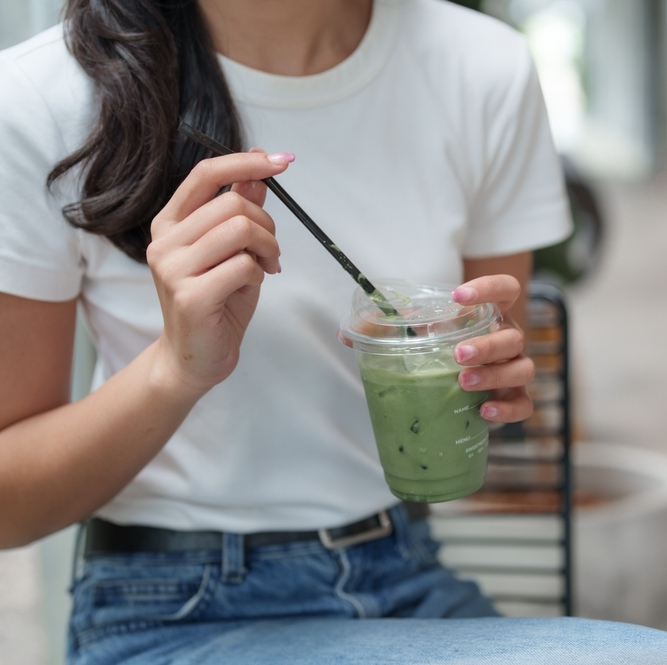 A photo of a woman drinking an iced matcha