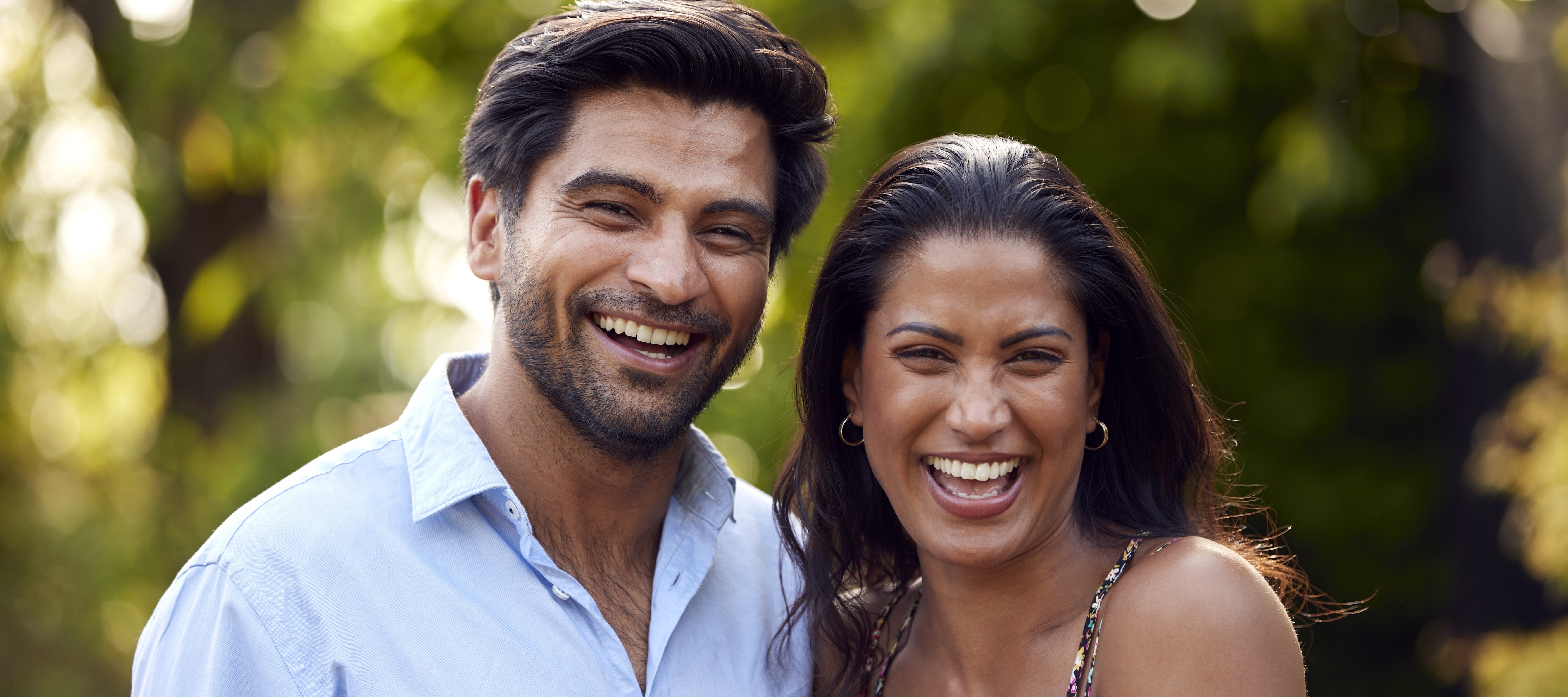 A happy couple smiles for the camera a sunny day in an outdoor setting.