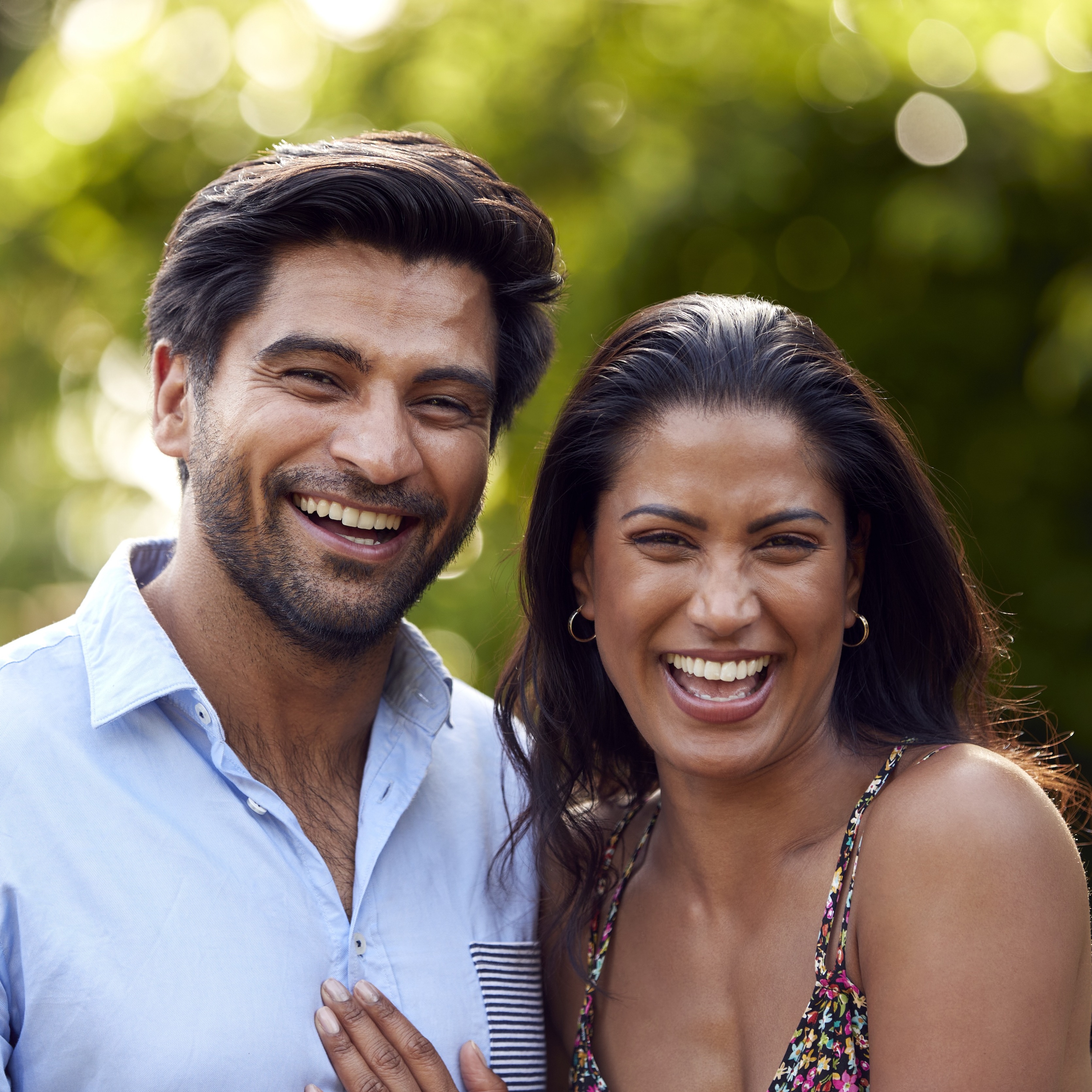 A happy couple smiles for the camera a sunny day in an outdoor setting.