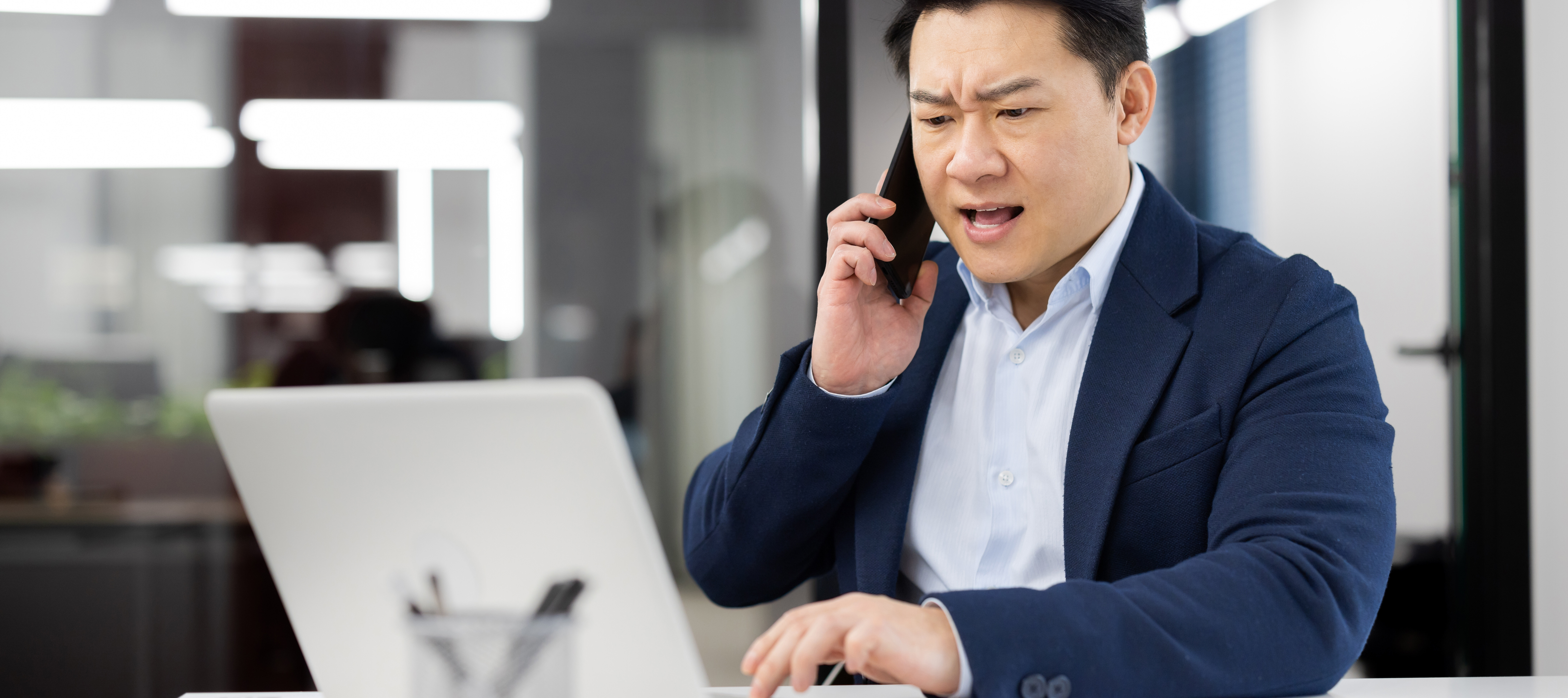 An angry man speaking on the phone while looking at his computer.