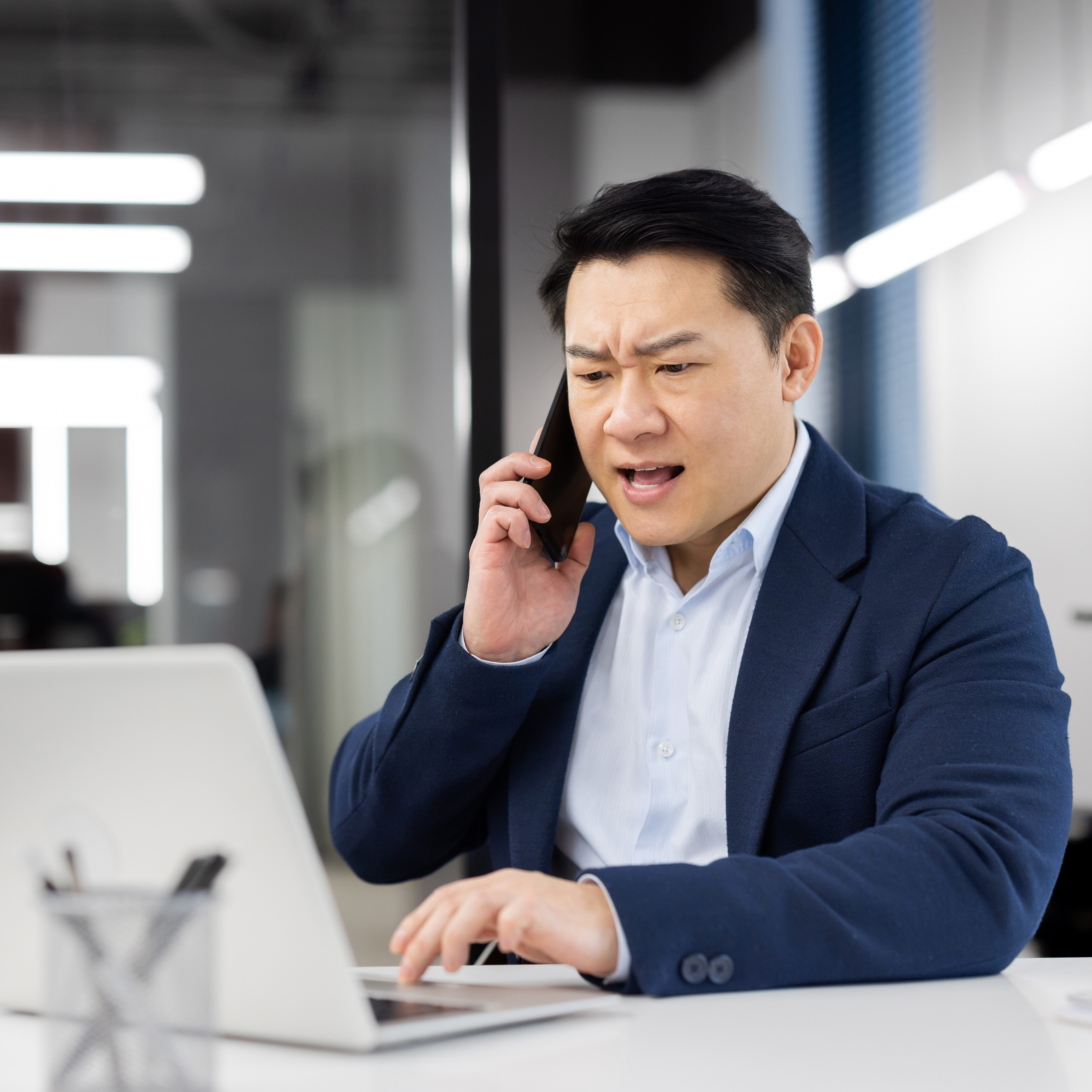 An angry man speaking on the phone while looking at his computer.