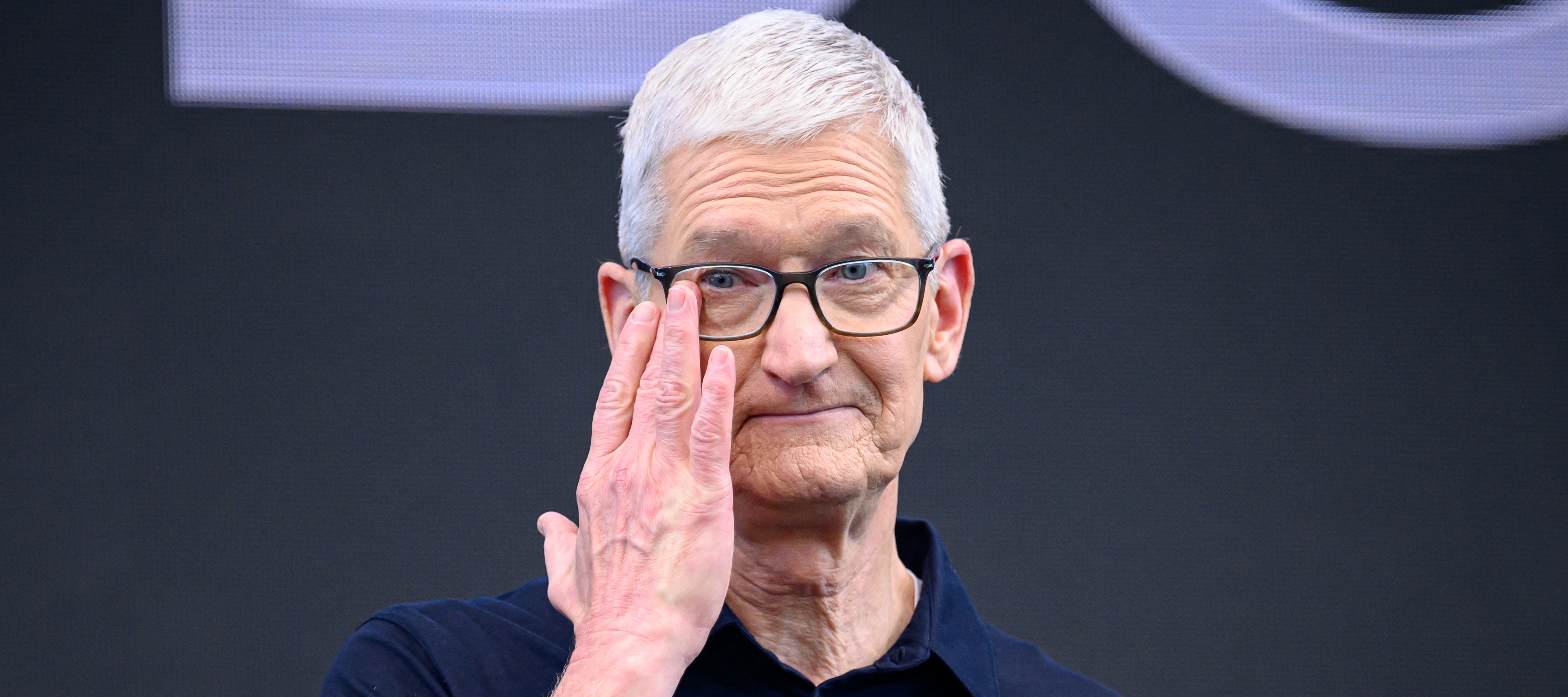 Tim Cook pushes up his glasses, looking grim.