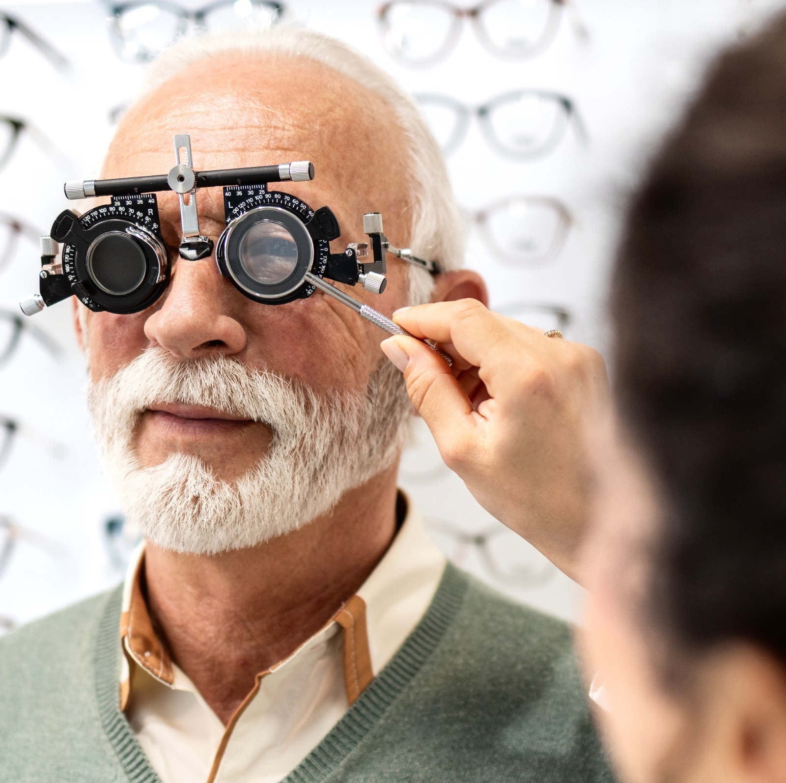 Professional ophthalmologist or optician testing senior man eyesight and diopter in eye clinic.