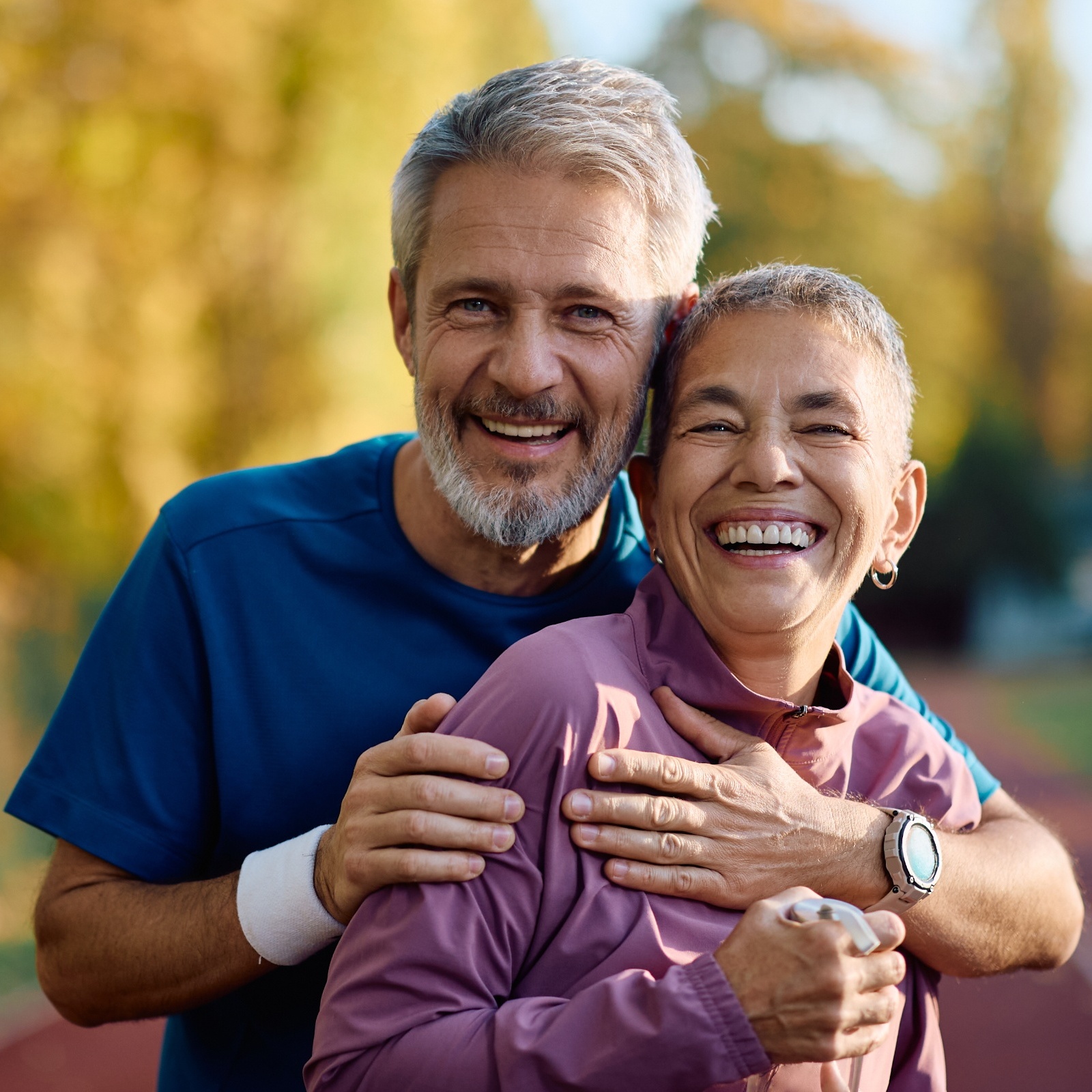Older couple smile for the camera, seen posing together in workout clothes at an outdoor track.