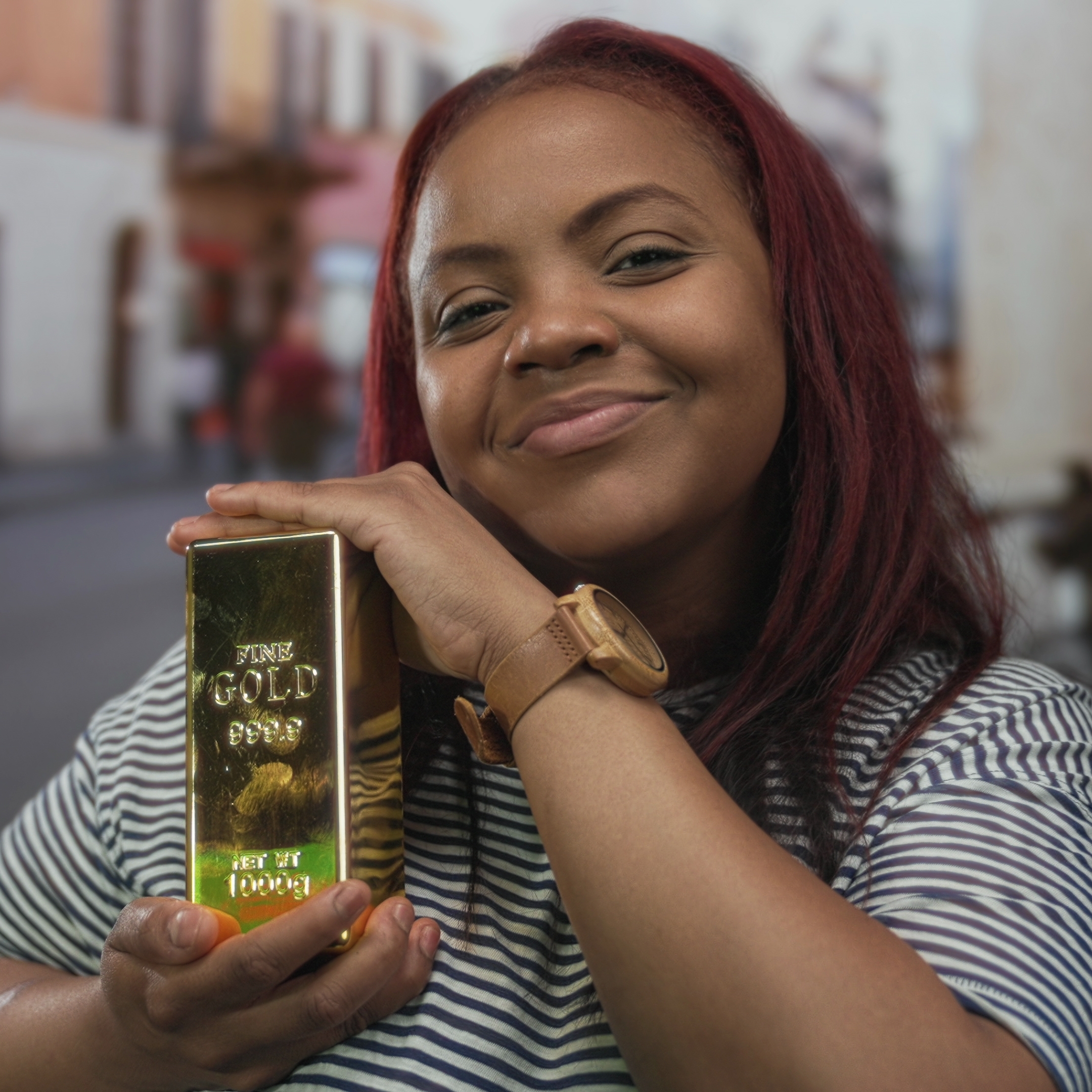 A woman holds a gold bar with both hands on busy crowded city street; she is happy and smiling broadly.
